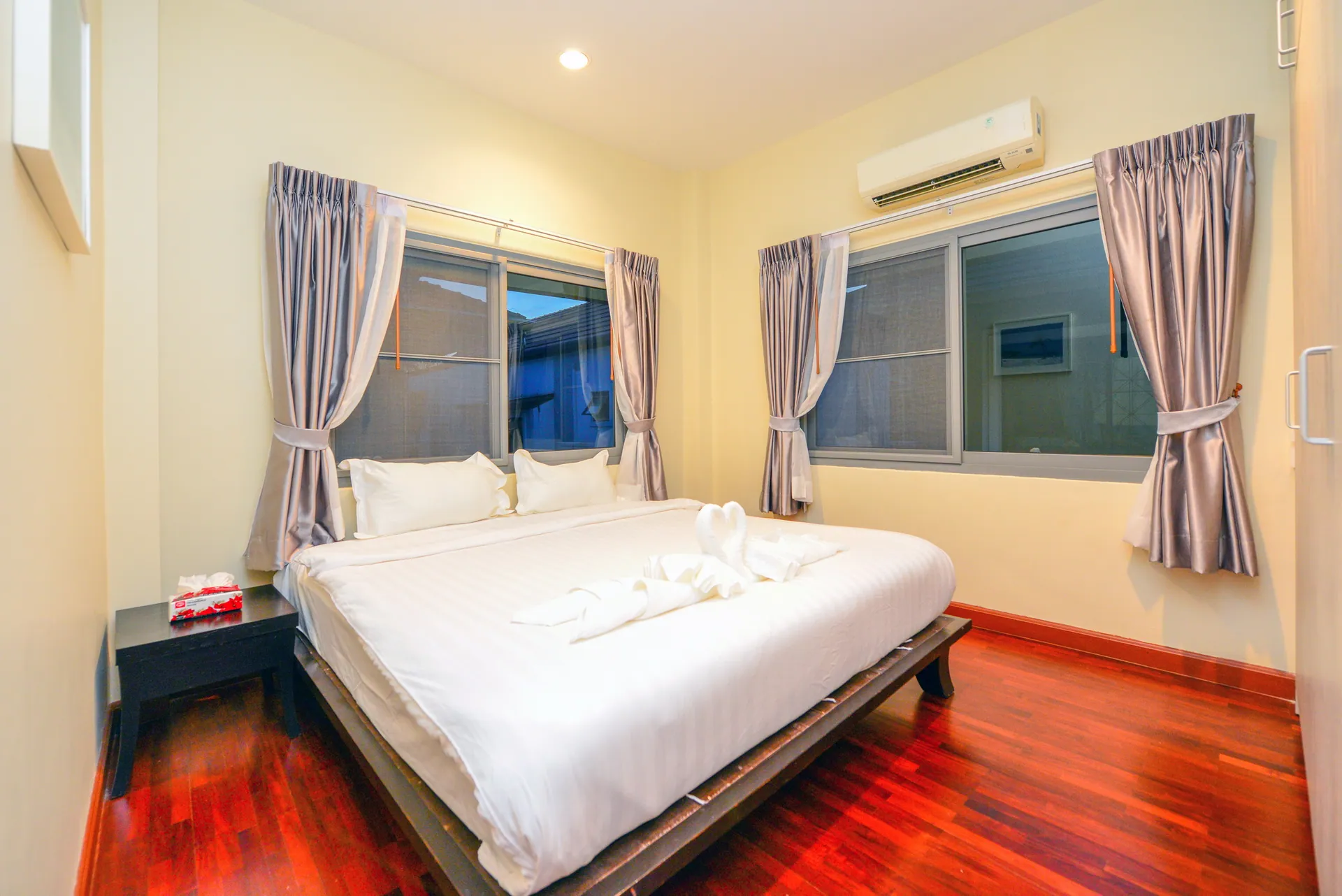 Bedroom with a king bed, a red timber floor and curtained windows on two walls