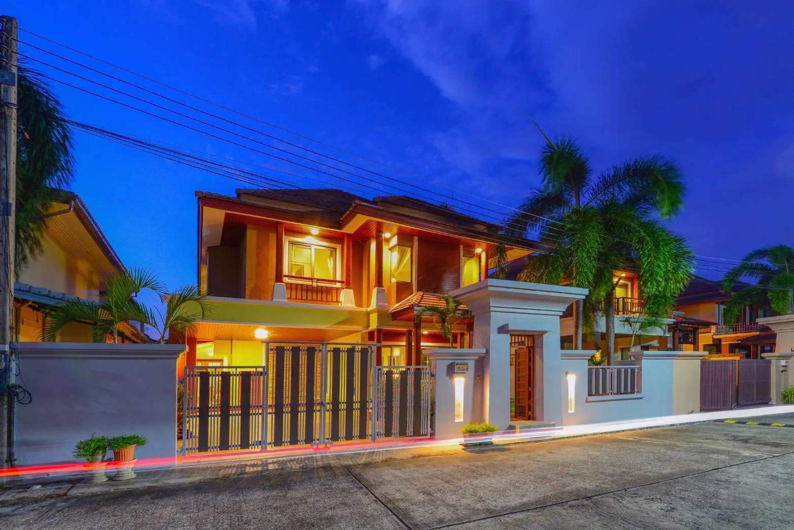 Two-storey villa with lit windows behind a white gated wall at dusk