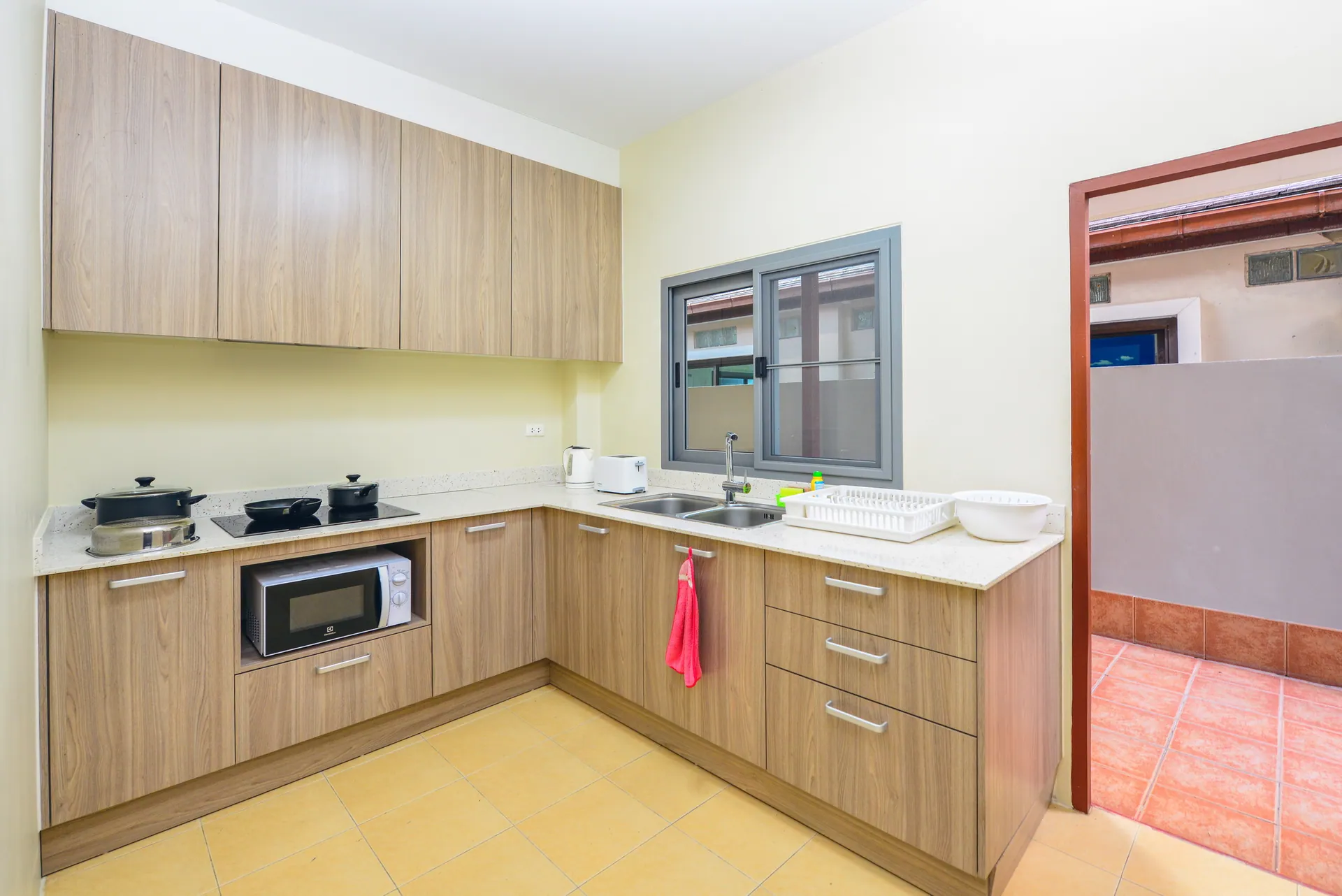 L-shaped kitchen with wood-finish cabinets, a hob, a microwave and a window over the sink