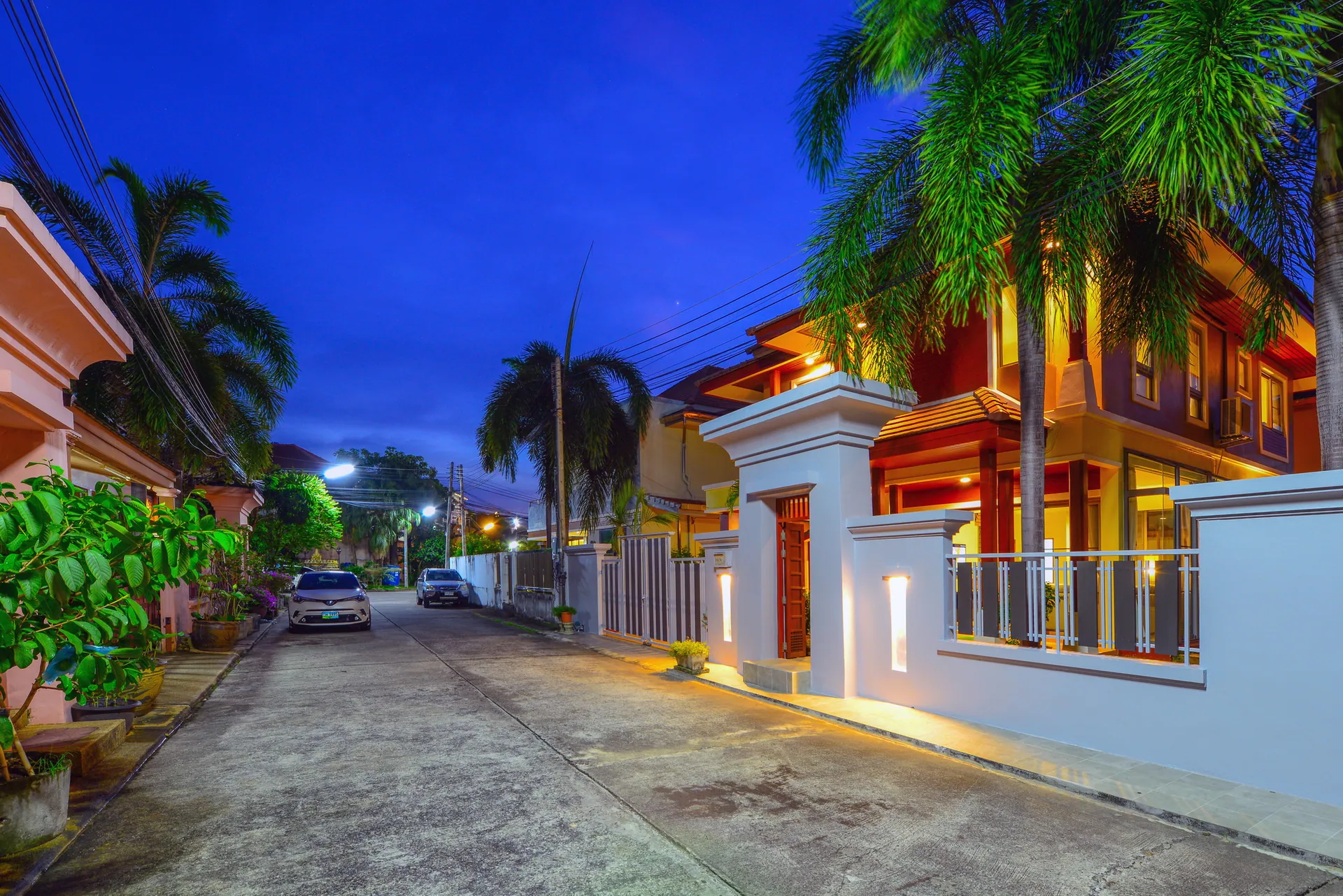 Quiet lane inside the gated community at dusk, lined with palms and garden walls