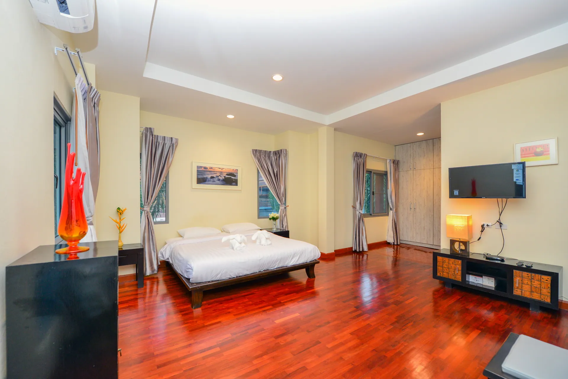 Large bedroom with a king bed, a wall-mounted TV and a red timber floor