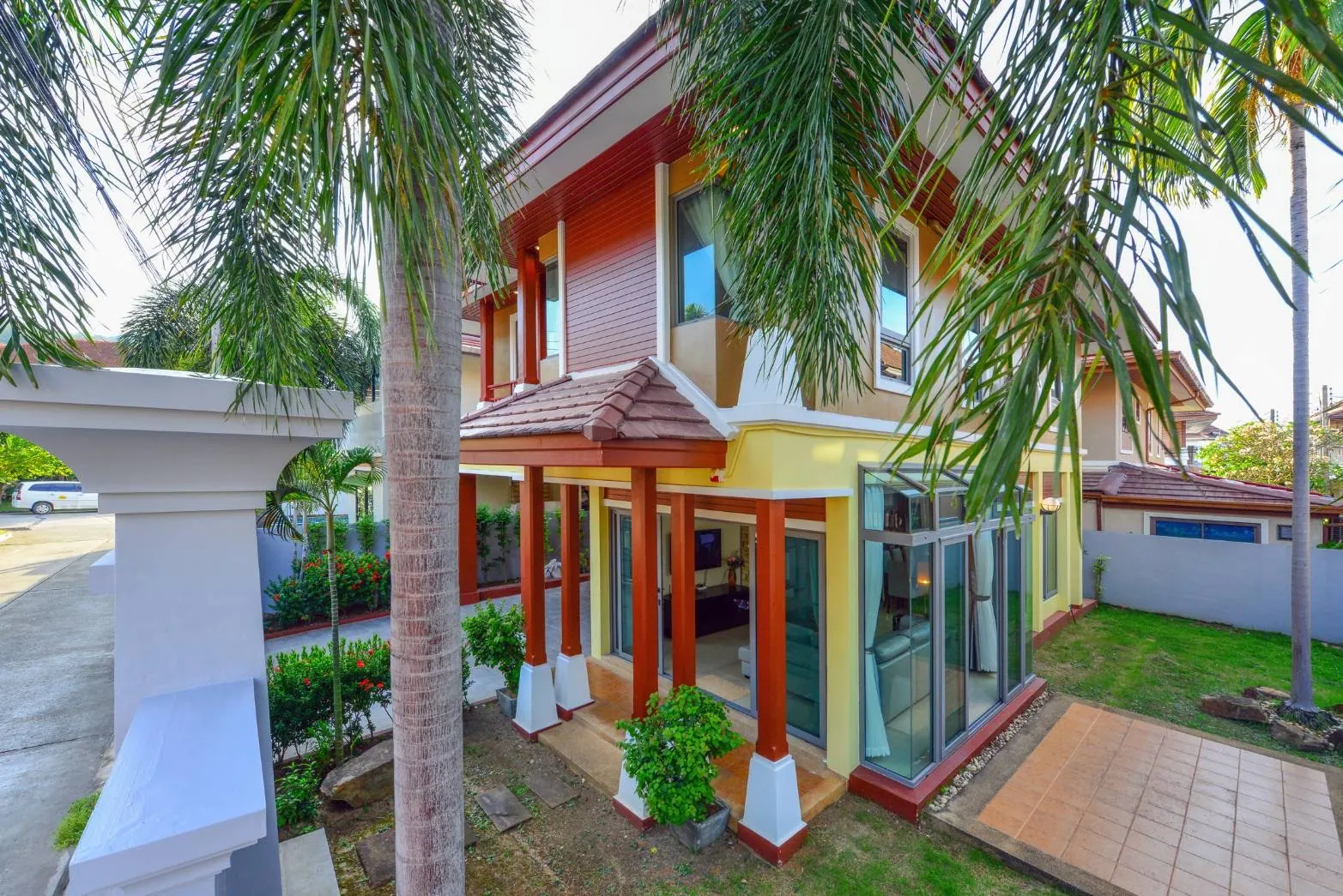 Side garden with palms, a lawn and a covered porch outside the glass-walled living room