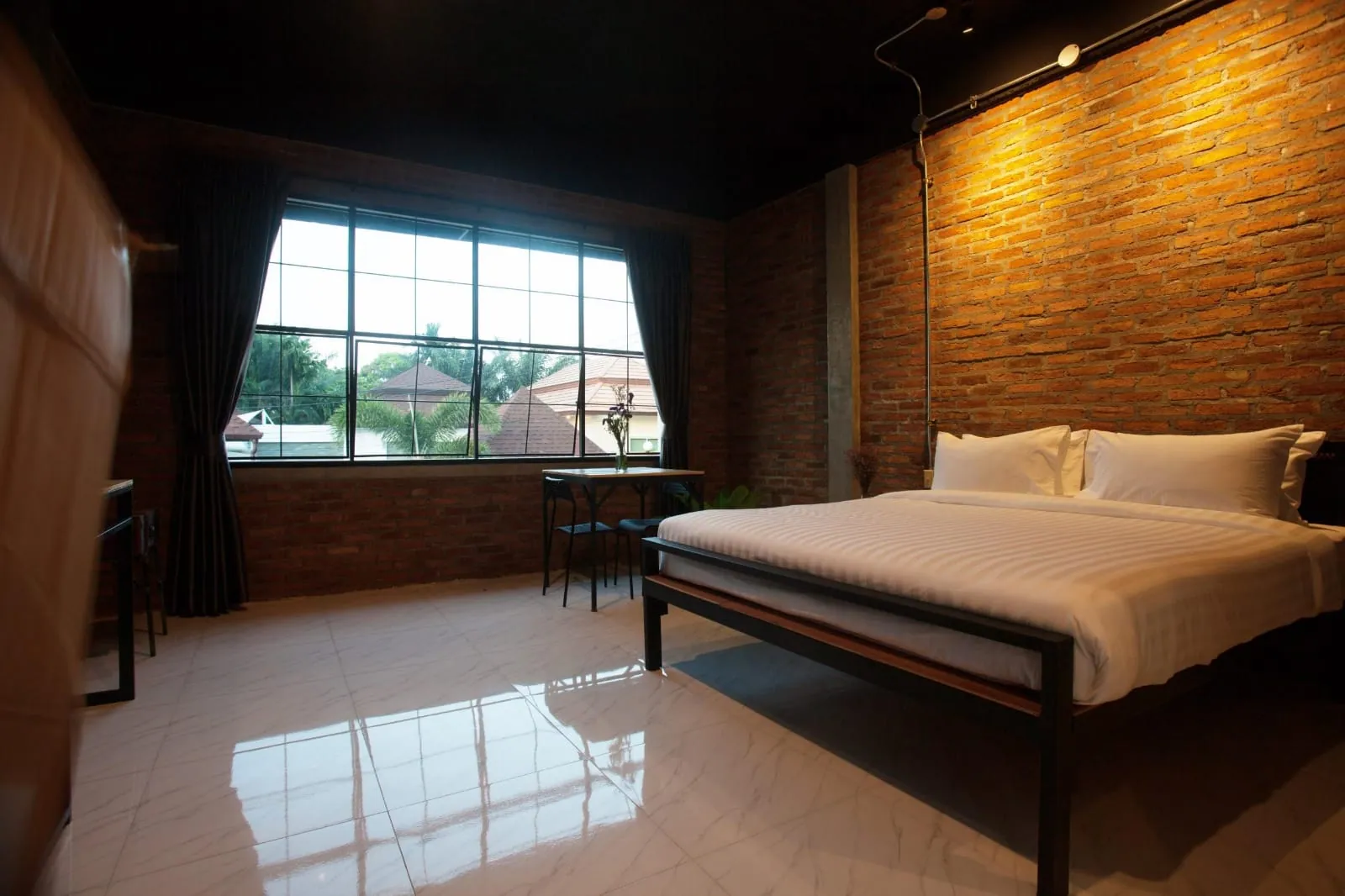 King bedroom with a large steel-framed window and a warm brick wall