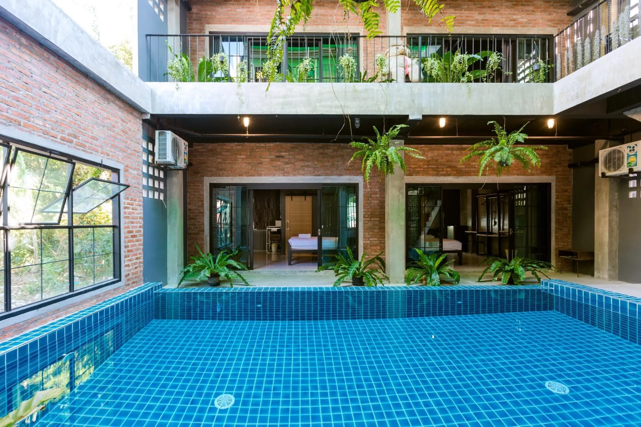 Courtyard pool framed by red brick walls, with ground-floor bedrooms opening onto the water and planted balconies above