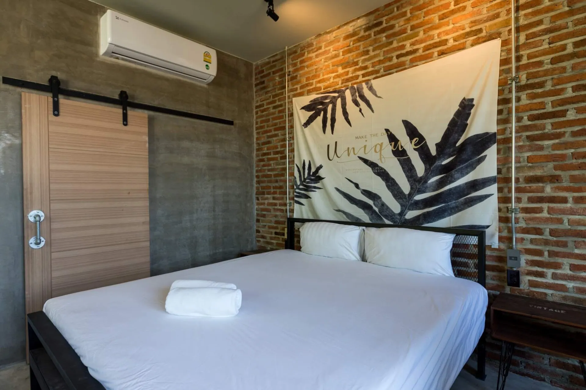 King bed below a palm-leaf print on an exposed brick wall