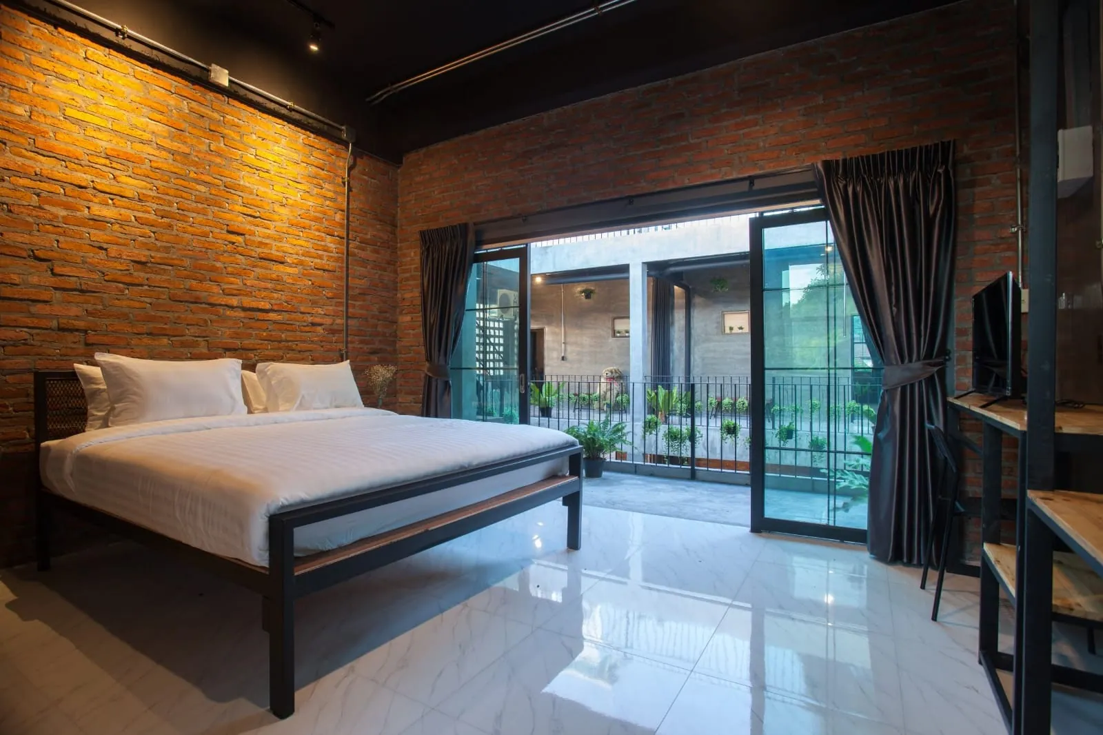 Brick-walled king bedroom with glass doors to a planted balcony