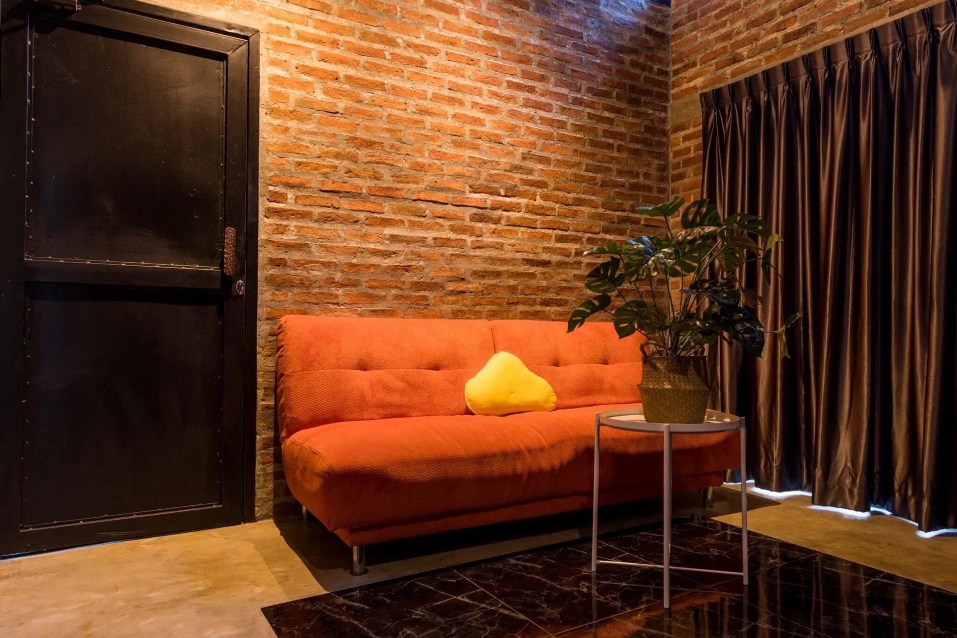 Orange sofa in the lounge of the loft bedroom, against exposed brick and dark curtains