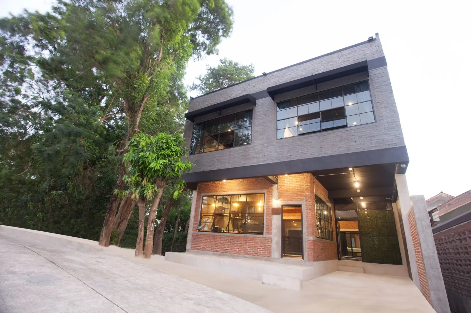Street facade in red brick and dark cladding with steel-framed windows, lit at dusk