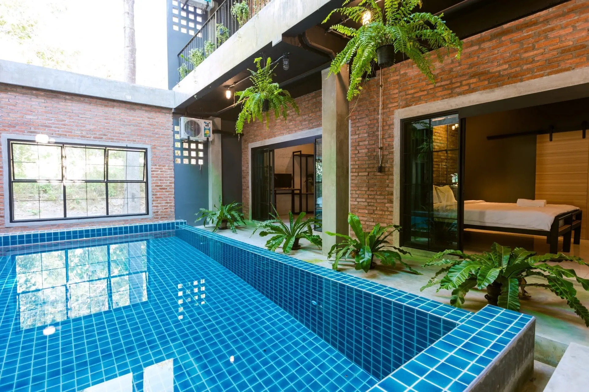Blue-tiled pool beside a steel-framed window wall, with a bedroom behind glass doors