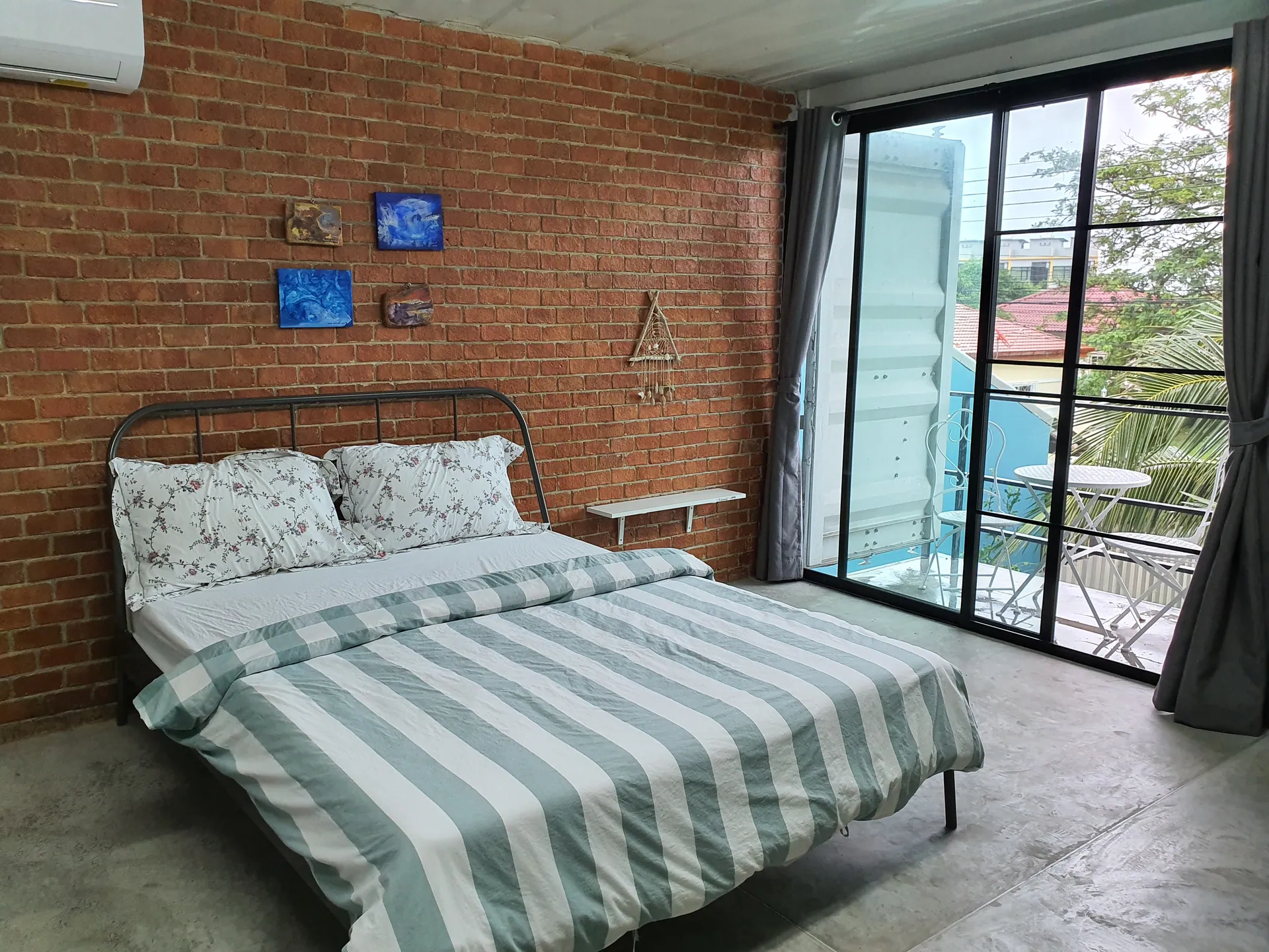 Double bed with striped linen against an exposed brick wall, beside glass doors to a balcony