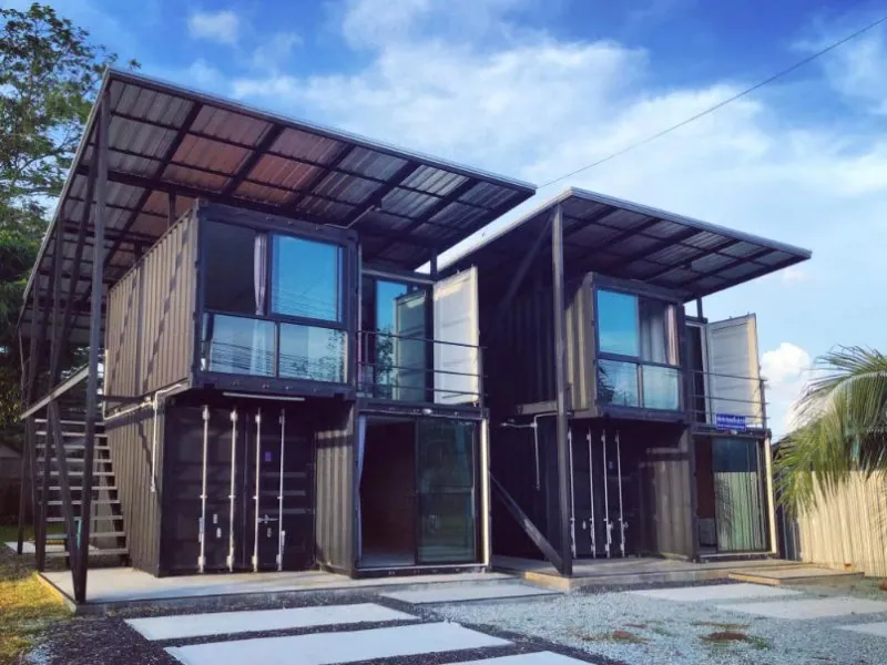 Two two-storey shipping-container blocks side by side beneath floating steel roofs, with glass doors below and balconies above