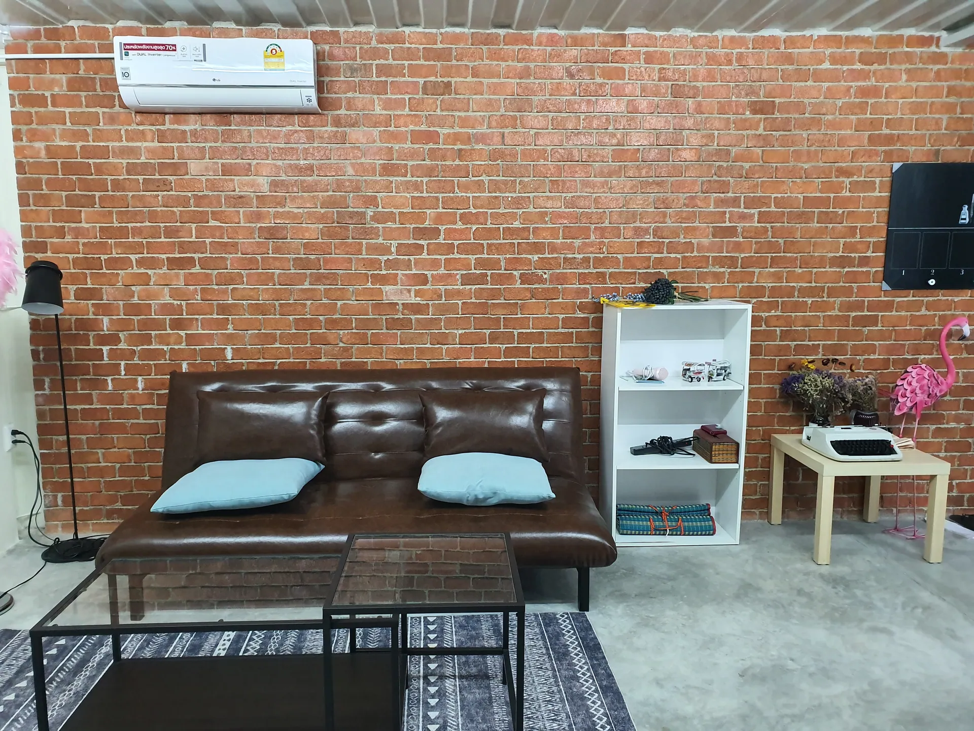 Lounge corner with a brown leather sofa, glass coffee table and white bookshelf against an exposed brick wall