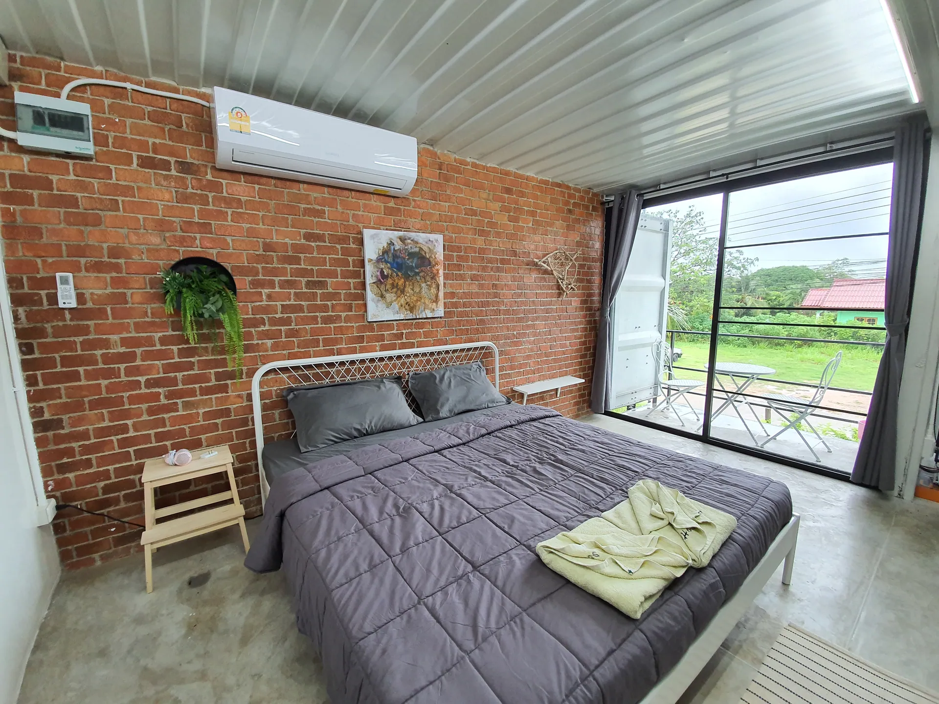 Double bed with grey linen against a brick wall, with sliding glass doors to a balcony and bistro table