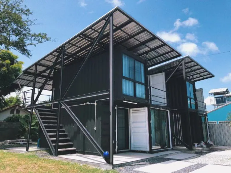 Black container block with an external steel staircase and a slanted steel roof against a blue sky