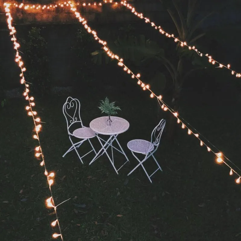 Bistro table and two chairs on the lawn at night, framed by strings of warm lights