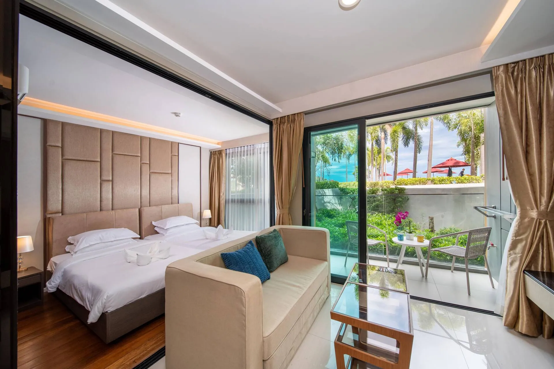 Twin beds and a sofa in an open-plan room, with glass doors to a garden terrace