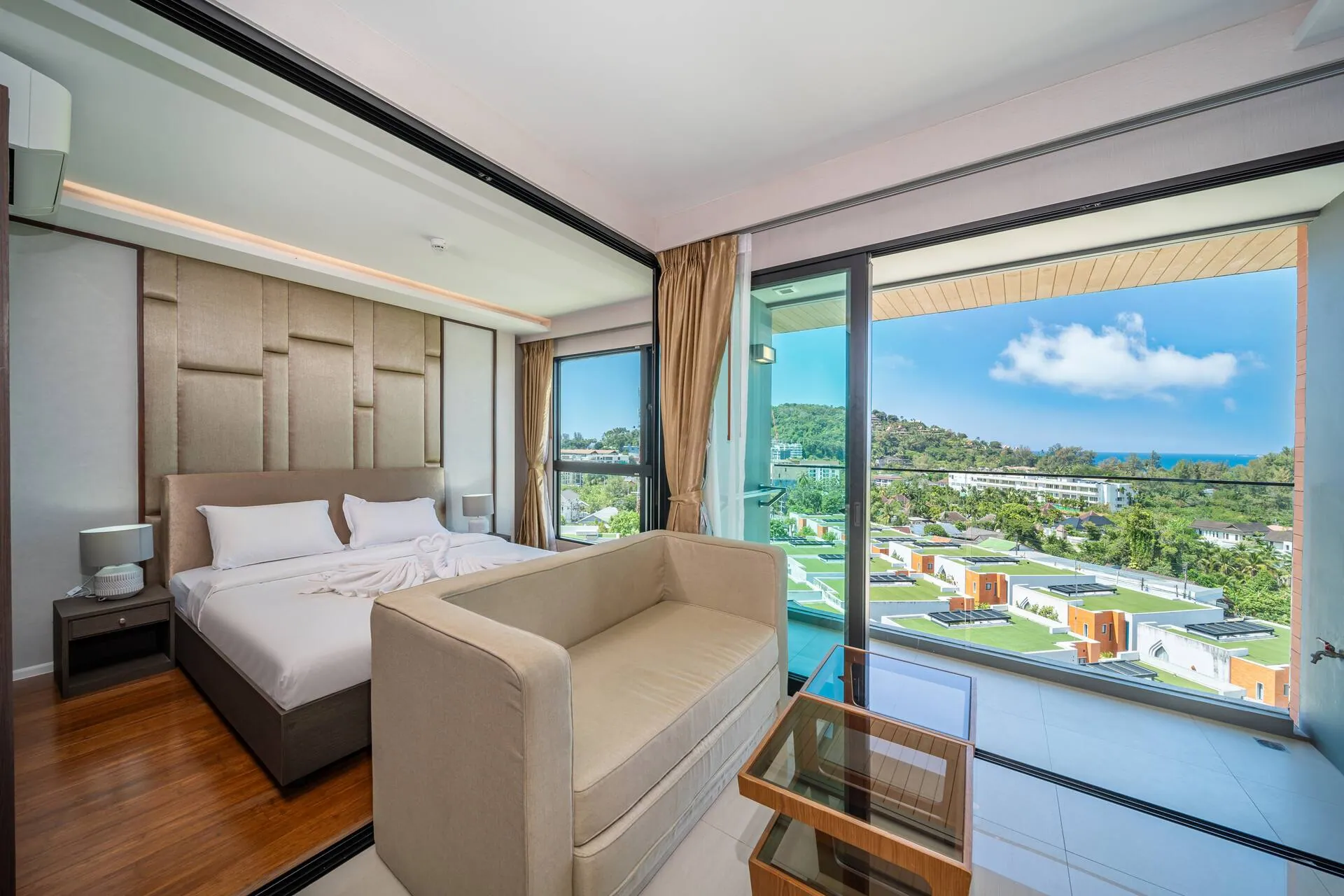 King bed and a sofa beside floor-to-ceiling windows, looking over the resort toward the sea