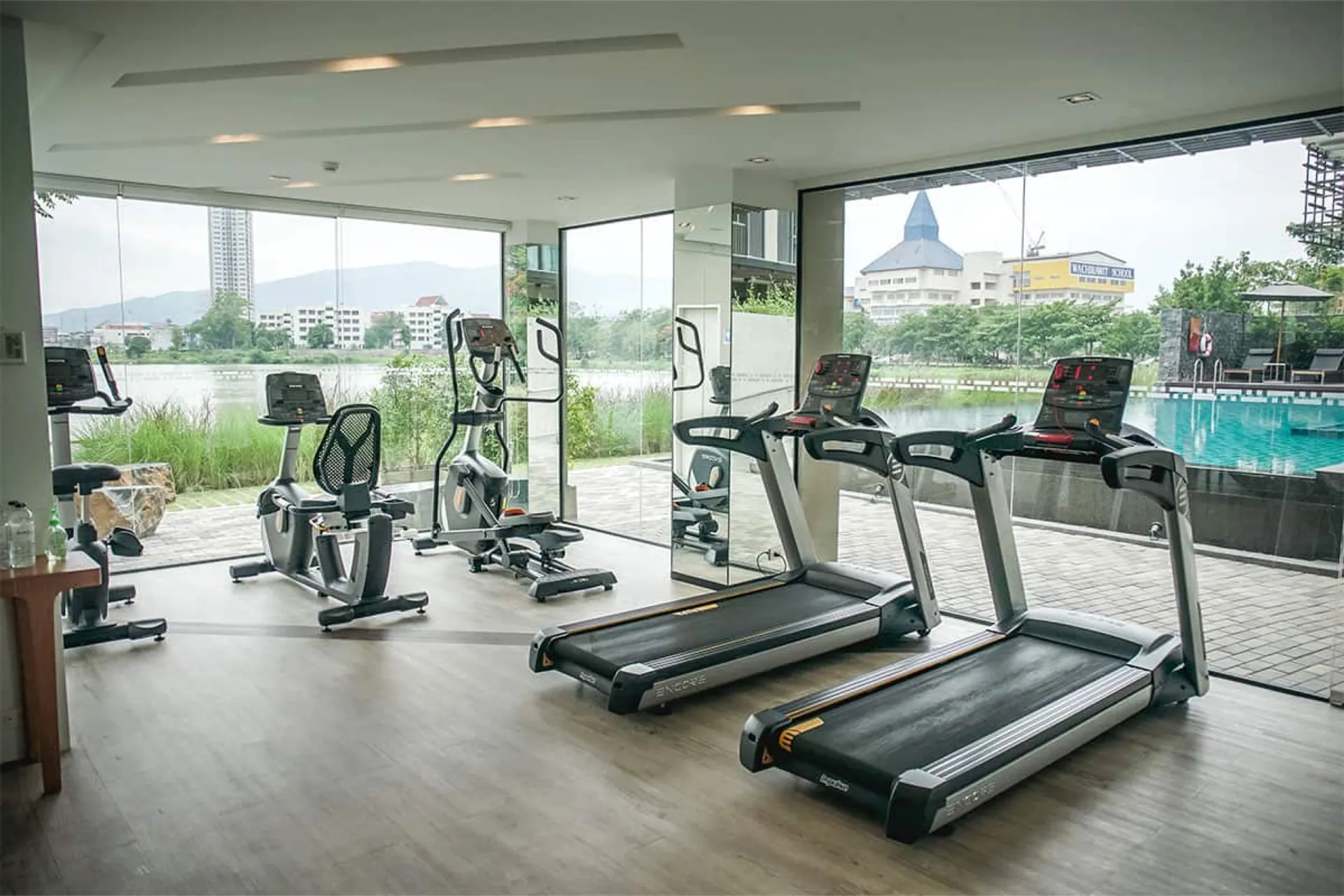 Fitness room with treadmills and cross-trainers behind floor-to-ceiling glass, facing the pool