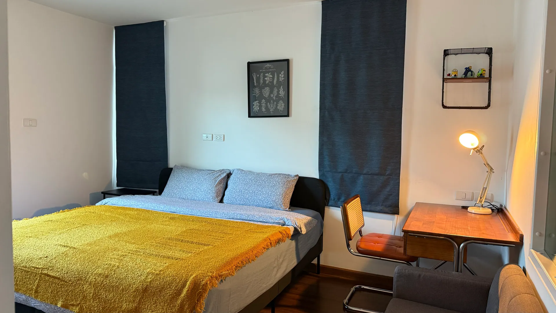Bedroom with a double bed under a mustard throw, a writing desk and a reading lamp