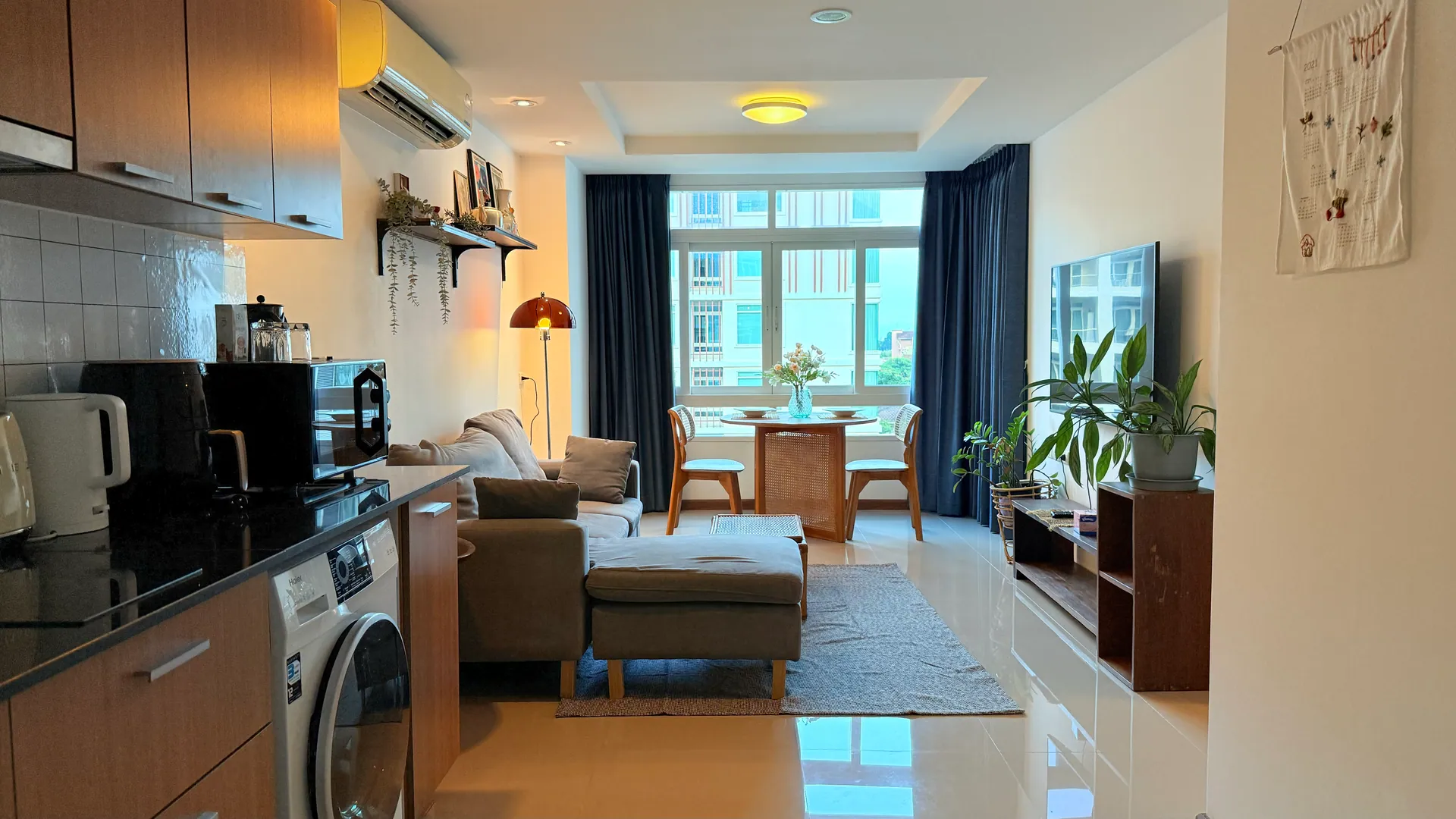 Open-plan kitchenette with a washing machine, leading through to the living area and windows