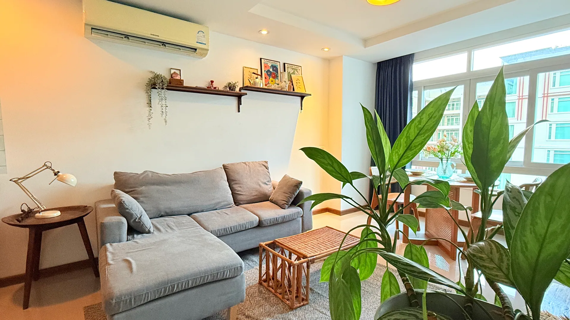 Living room with a grey corner sofa, a rattan coffee table and potted plants by the window