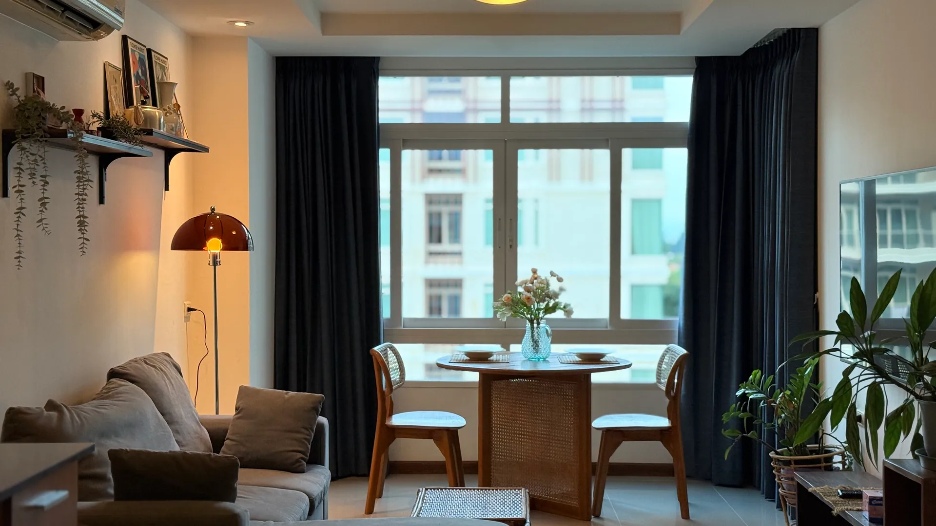 Living and dining area with a floor lamp, wall shelves and a round table at the window