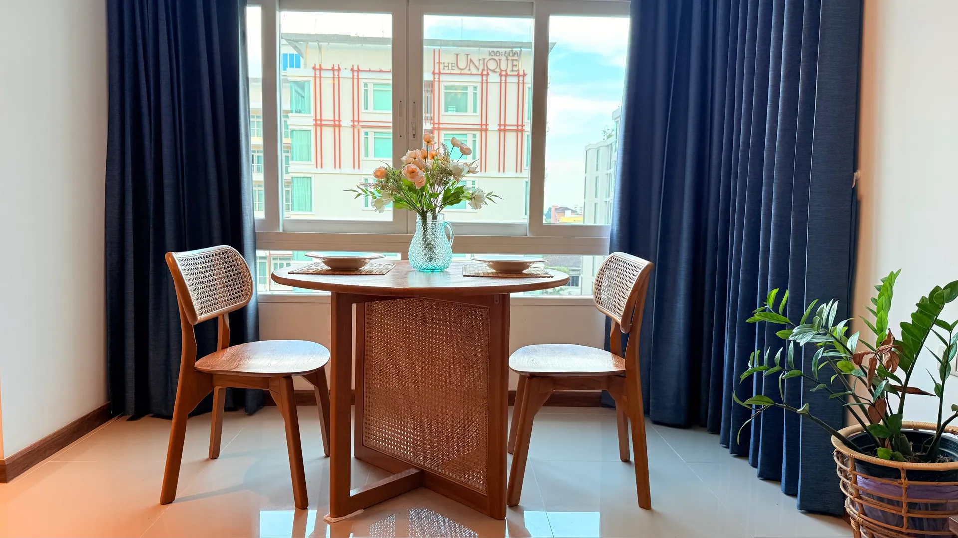Round timber dining table for two with cane-back chairs, framed by navy curtains