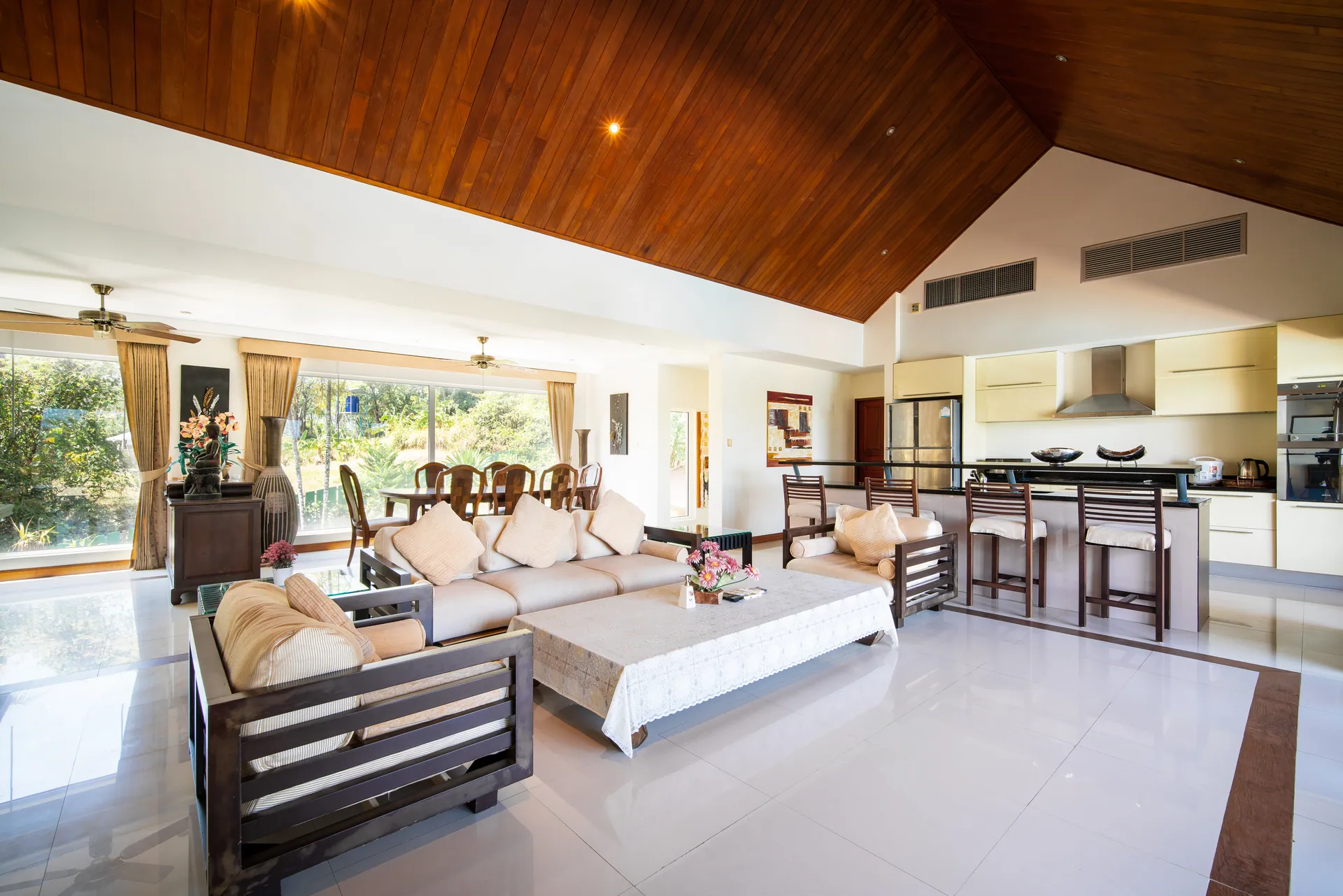 Open-plan living room under a vaulted timber ceiling, with sofas and a breakfast bar in front of the kitchen