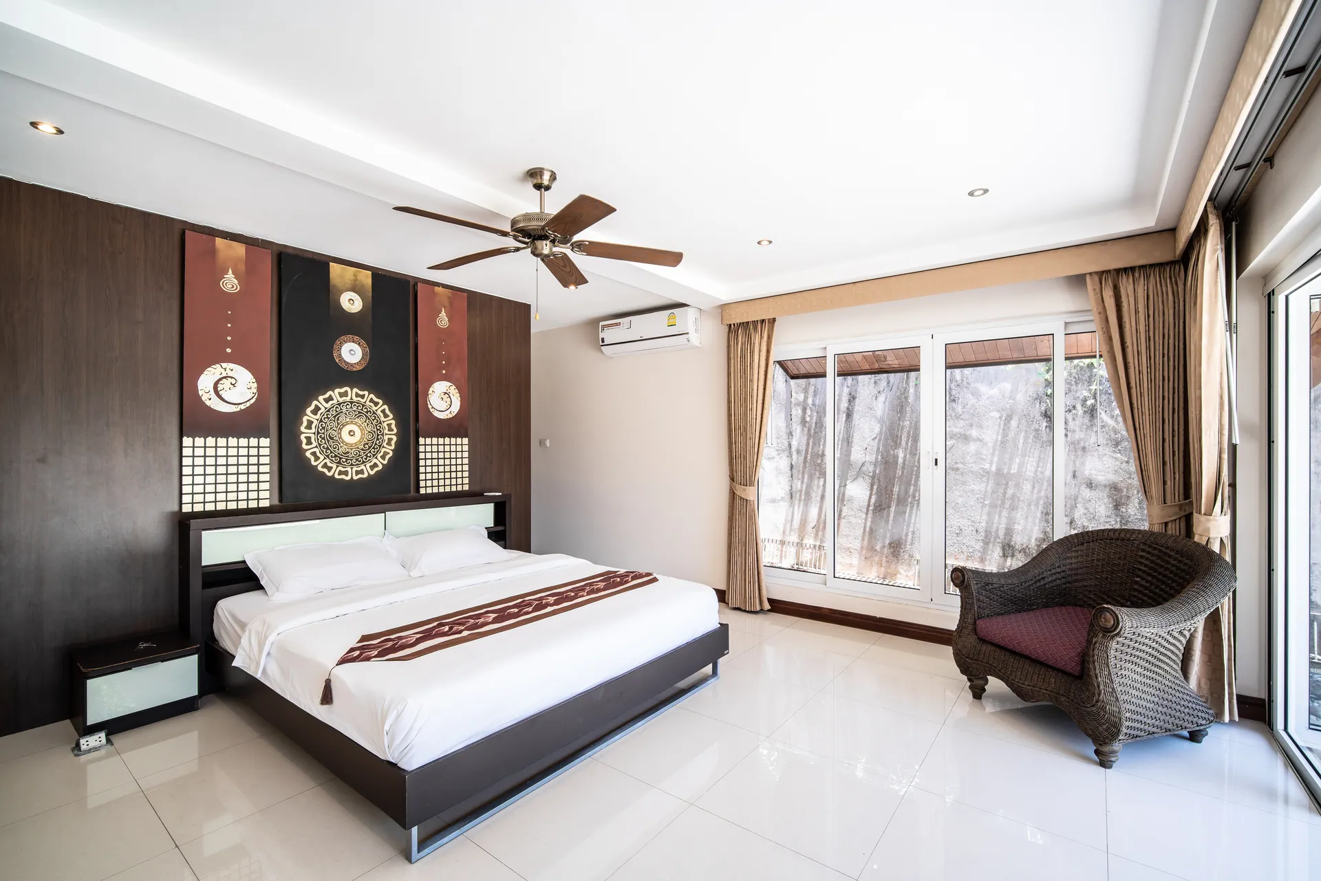 Bedroom 3 with a carved timber headboard wall, an armchair and garden-facing windows
