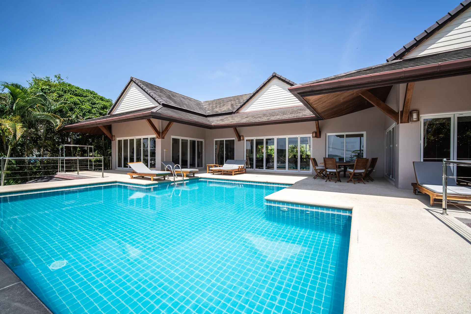Pool terrace with sun loungers in front of the single-storey pavilion and its tiled gabled roofs