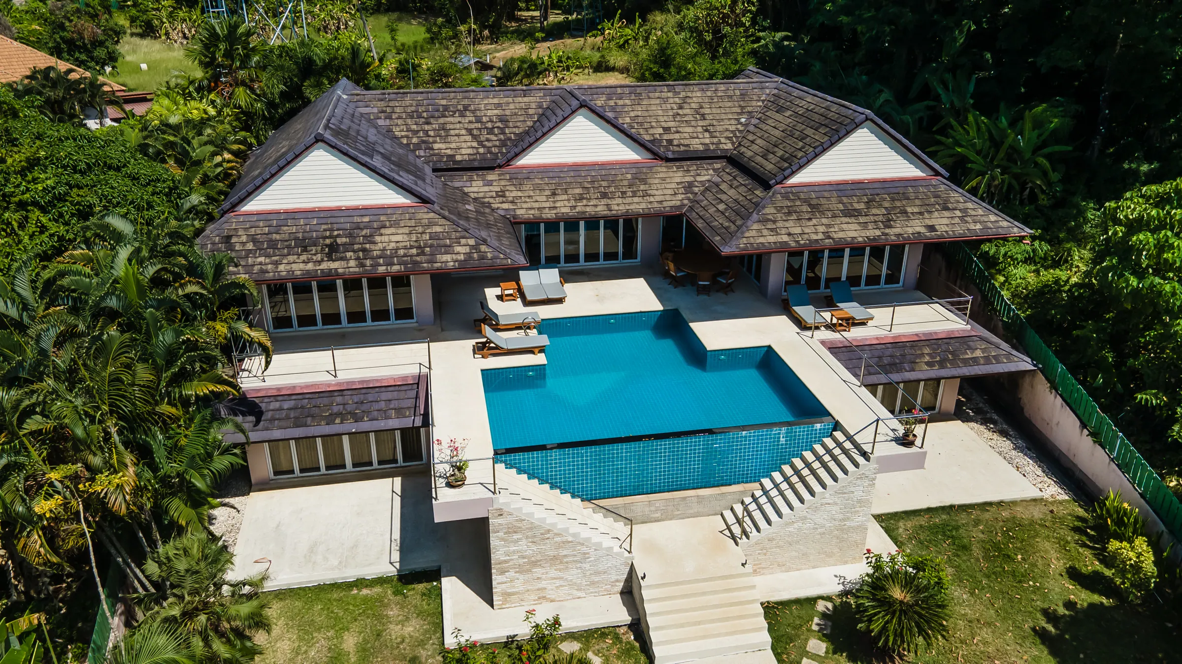 Aerial view of the villa's gabled roofs above a large pool terrace, with stone steps down to the garden