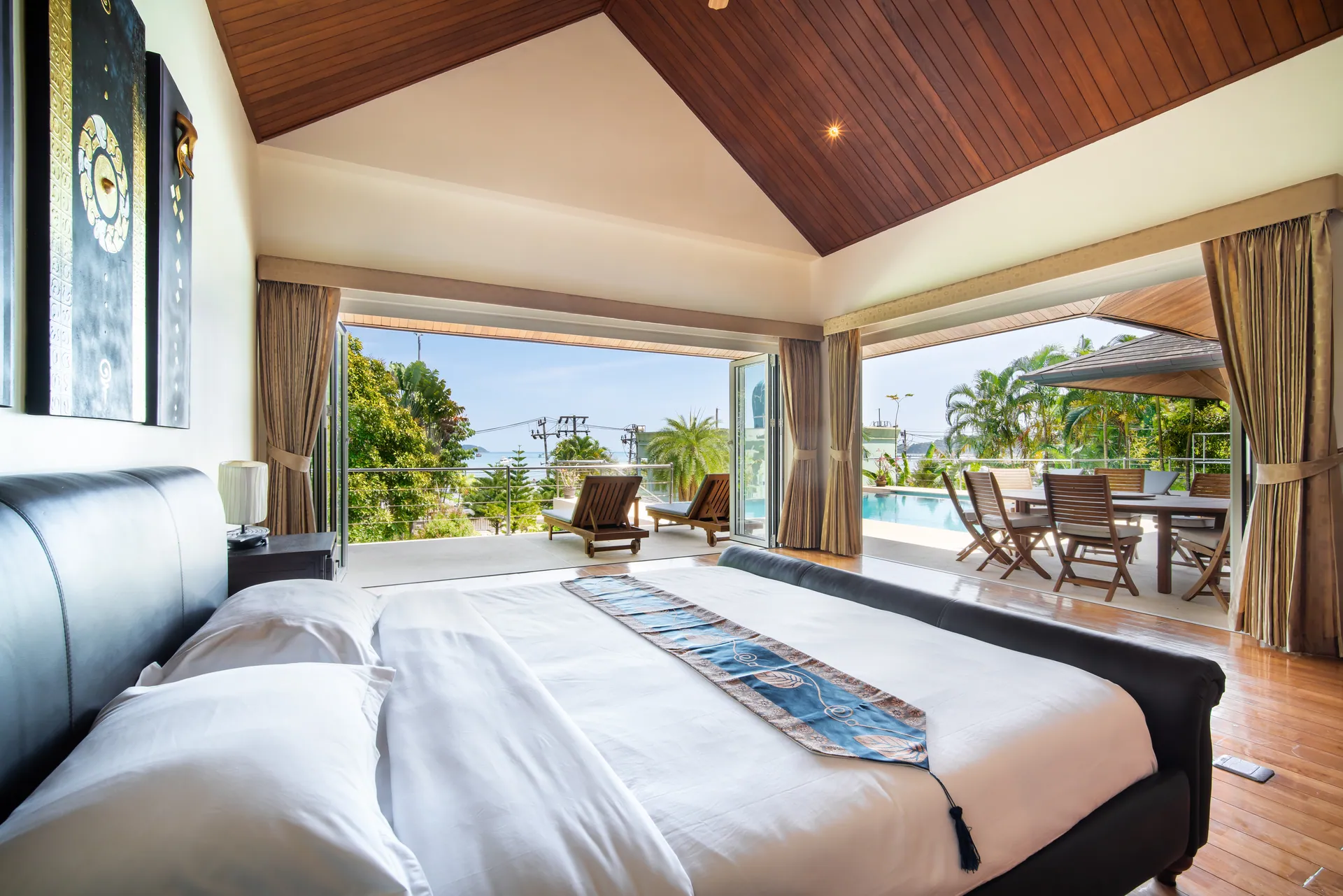 Bedroom 2 with its glass doors folded back to the pool terrace and the treetops beyond