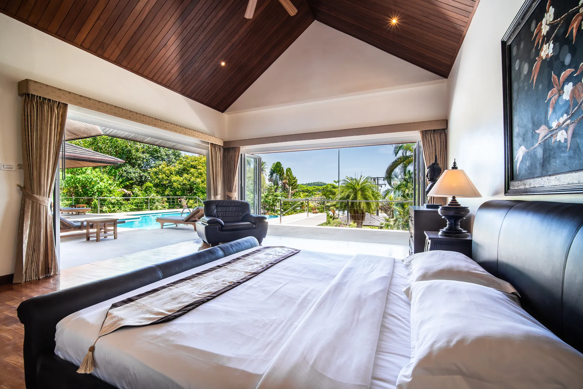 Bedroom 1 with a leather sleigh bed under a timber-lined vaulted ceiling, its glass doors open to the pool terrace