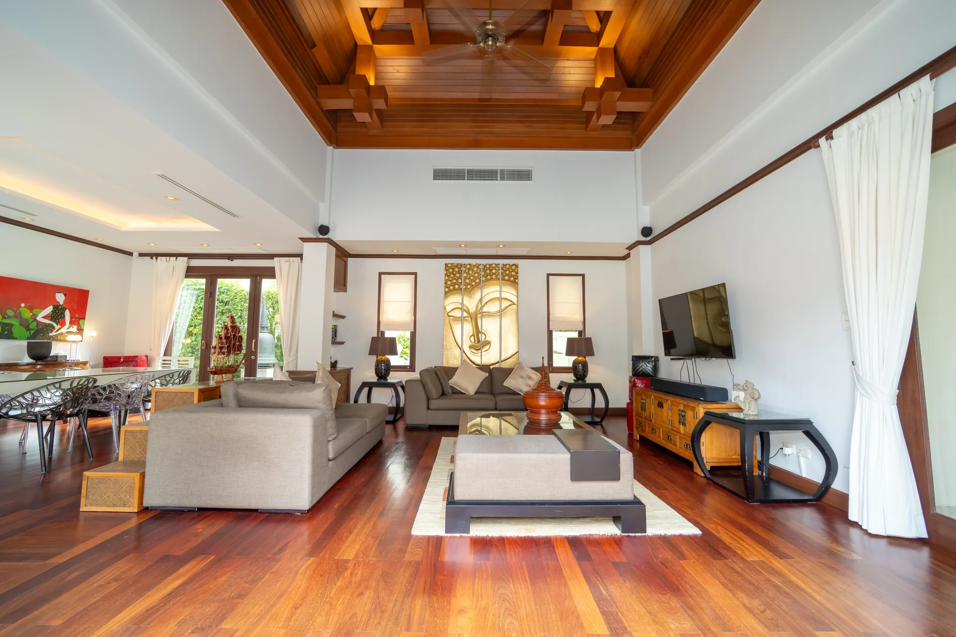 Living room under a carved timber ceiling, with sofas, a gilded Buddha panel and polished wooden floors