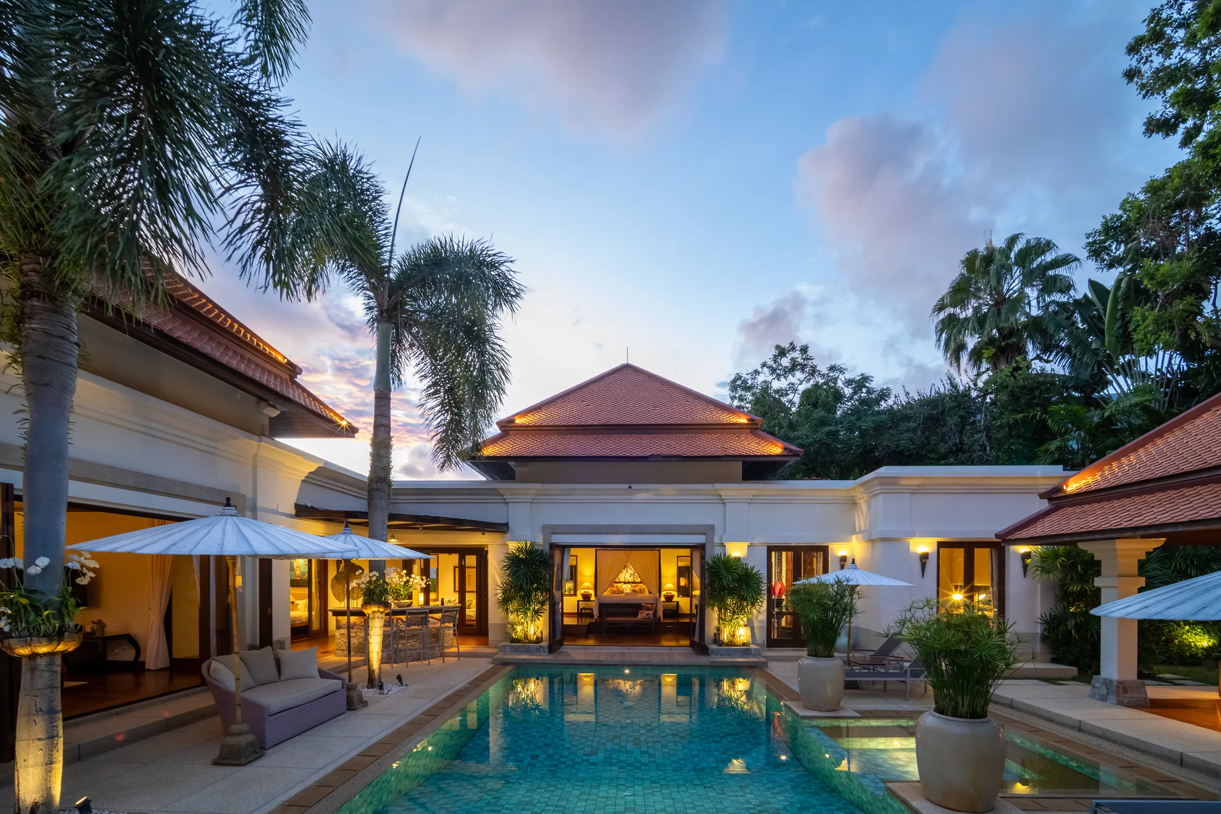 Courtyard pool at dusk, with the lit master bedroom opening onto the water beneath a terracotta pavilion roof