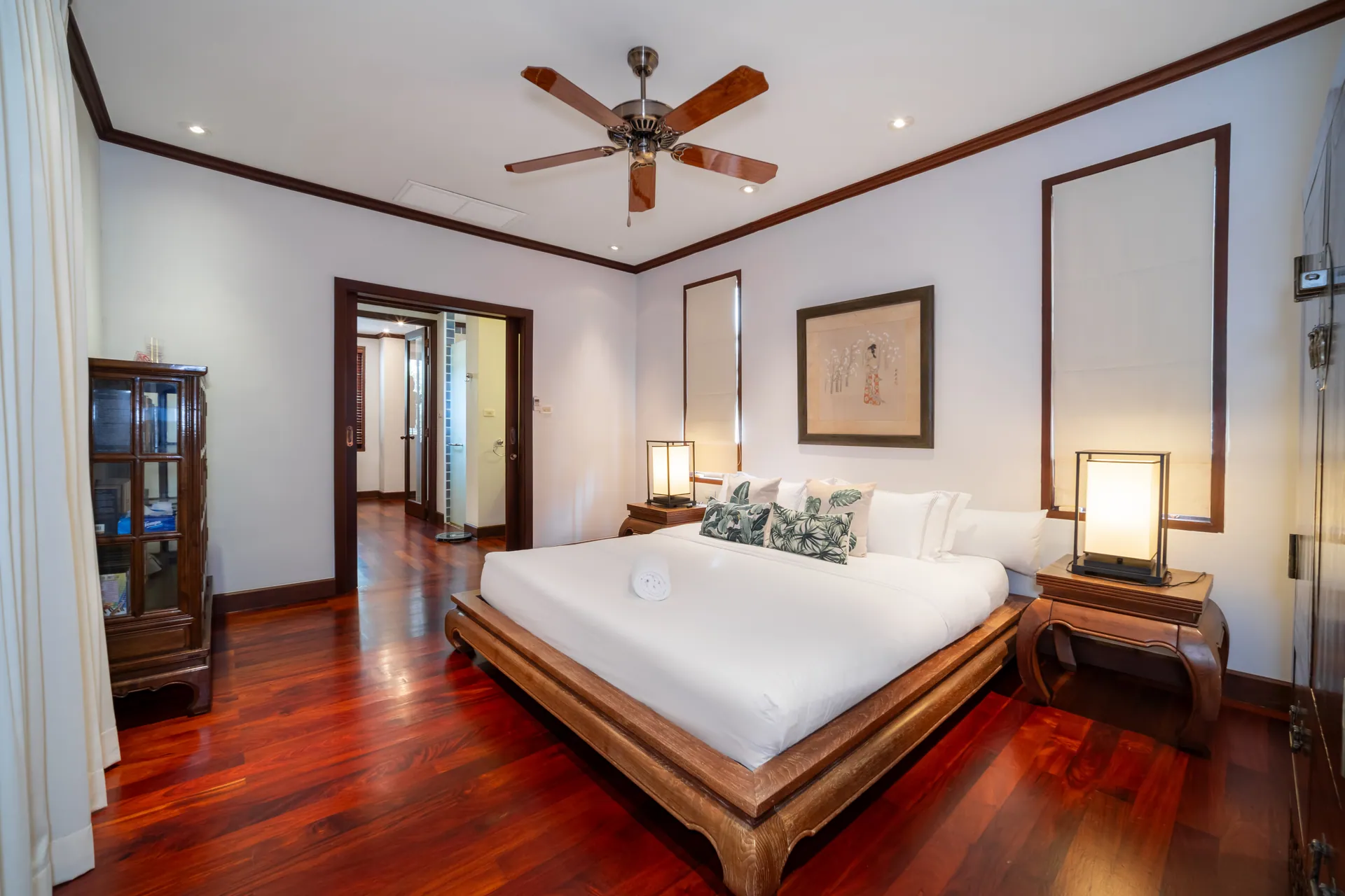 Bedroom with a large bed on a low timber frame, paper table lamps and a ceiling fan