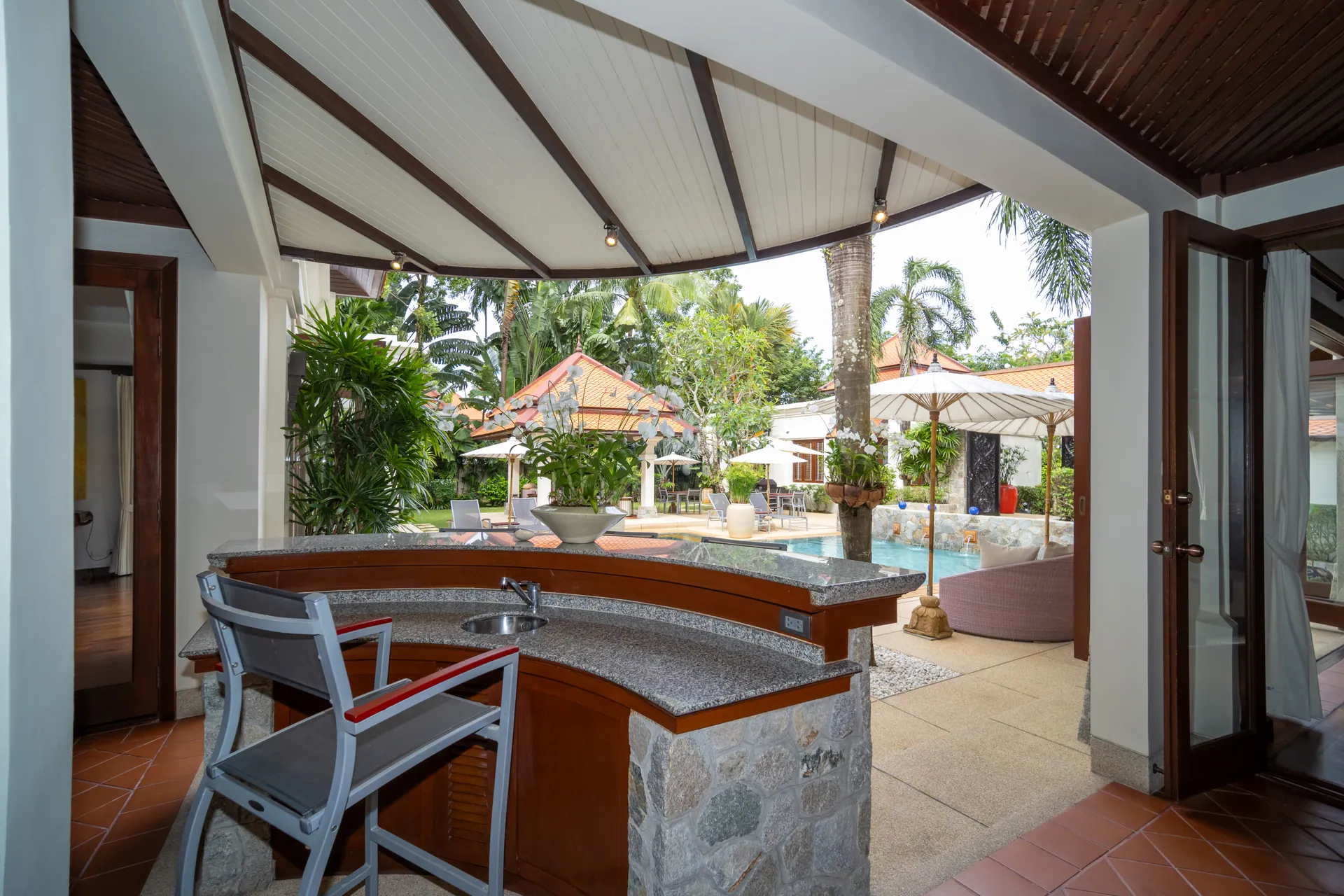Covered outdoor bar counter with stools, looking out across the terrace to the pool