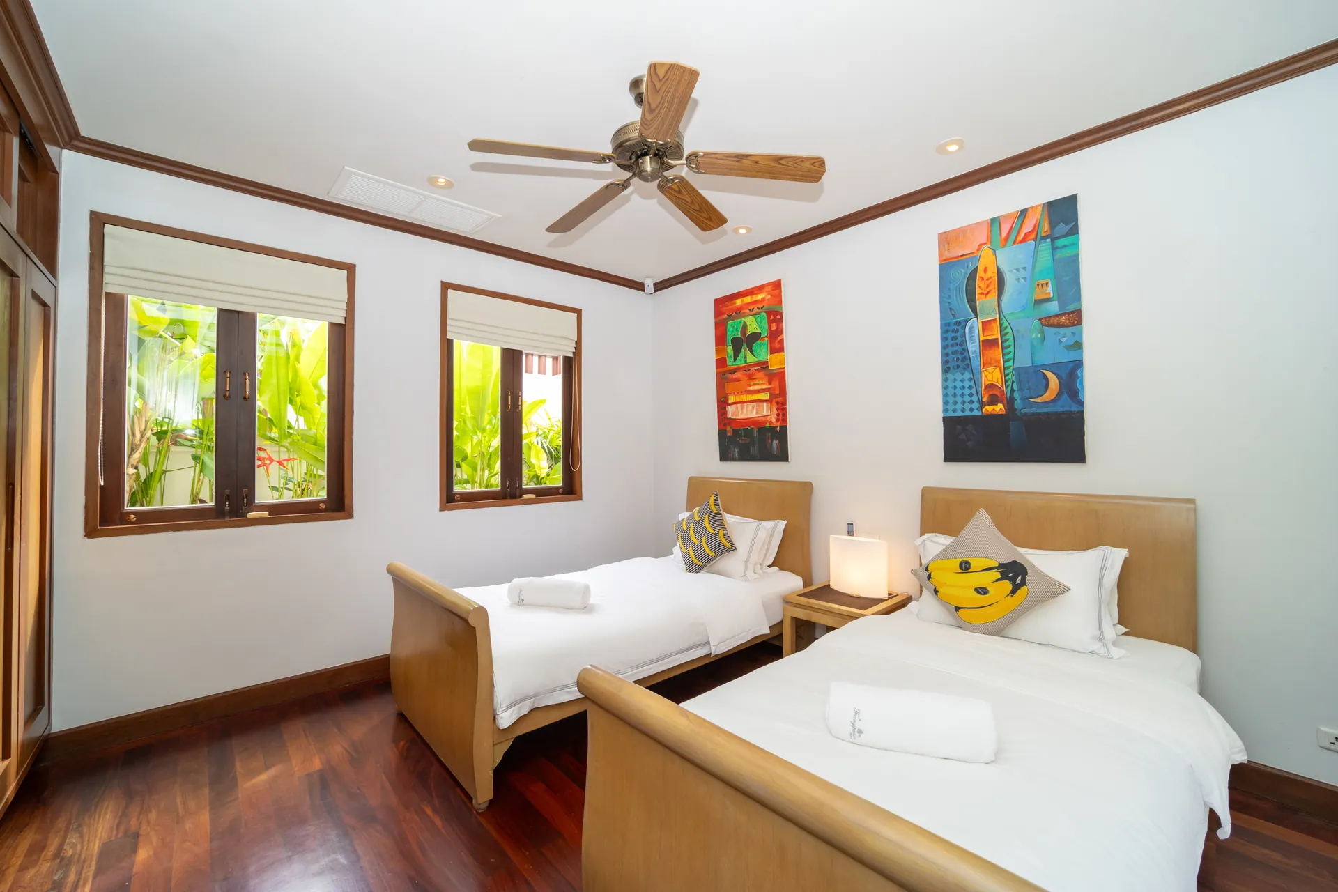 Twin bedroom with two single beds, bright artwork and a ceiling fan