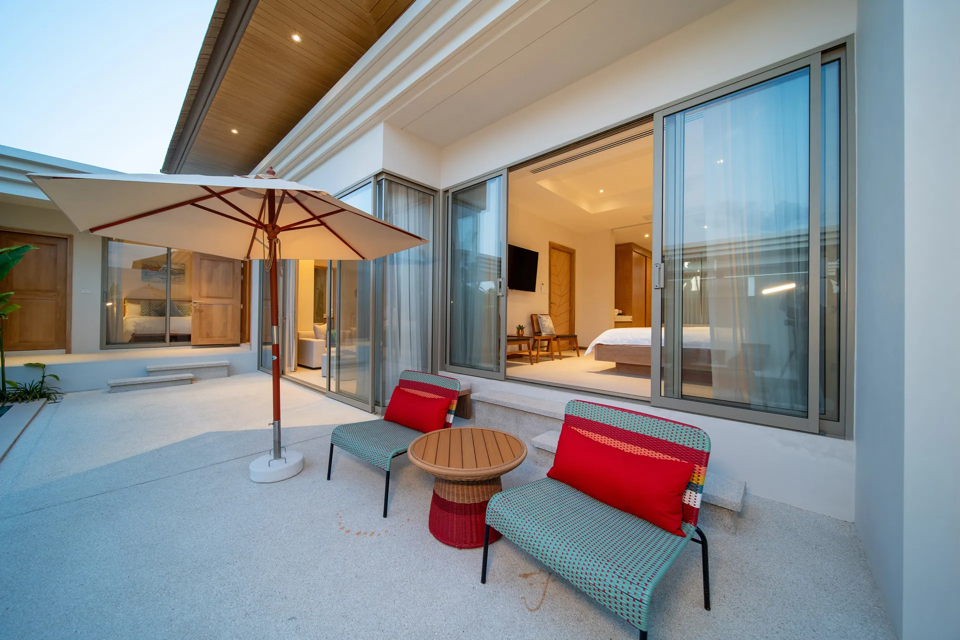Red-cushioned chairs and a side table under a parasol on the terrace outside the main bedroom