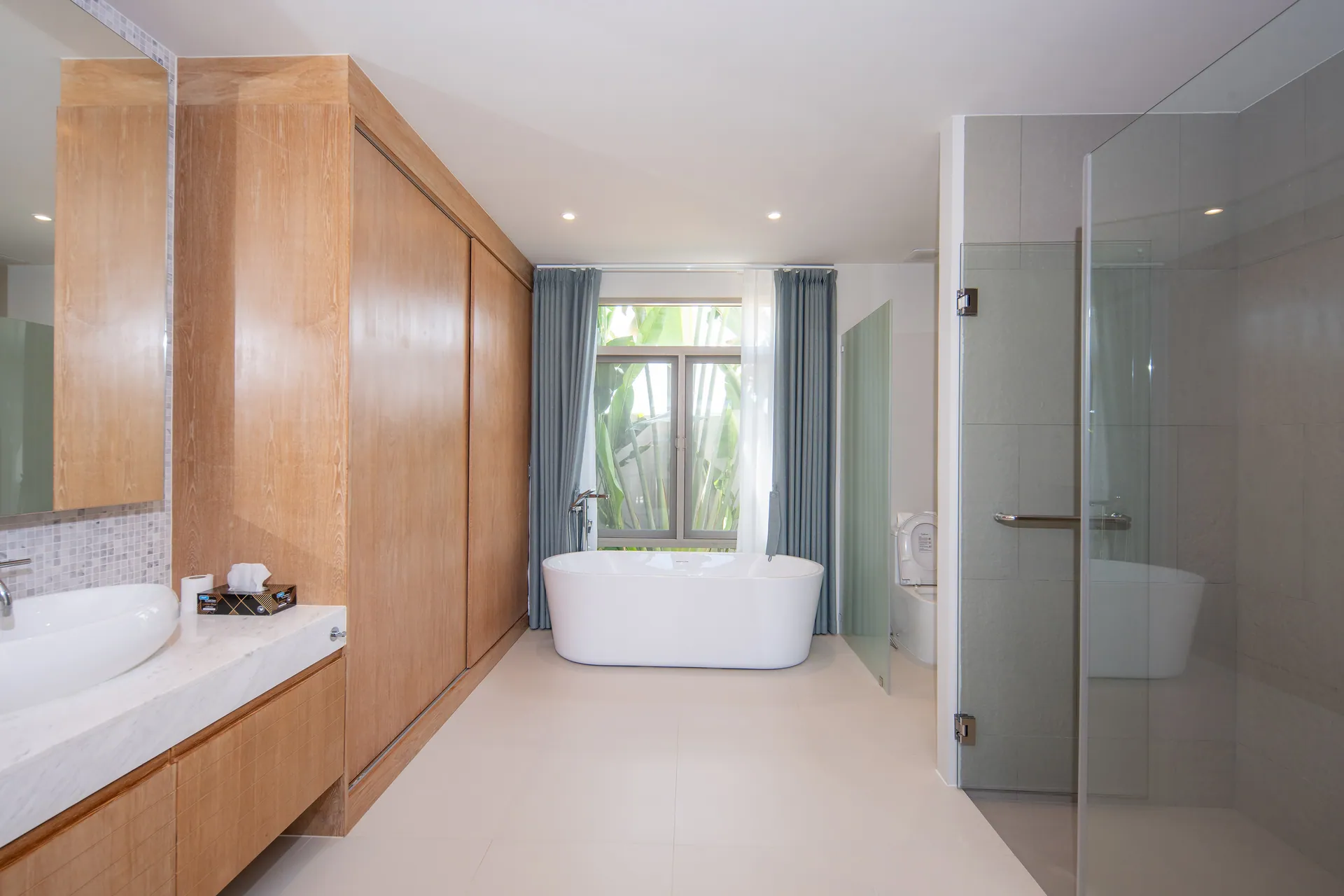 Main bathroom with a timber wardrobe wall, a freestanding bath beneath the window and a glass-screened shower