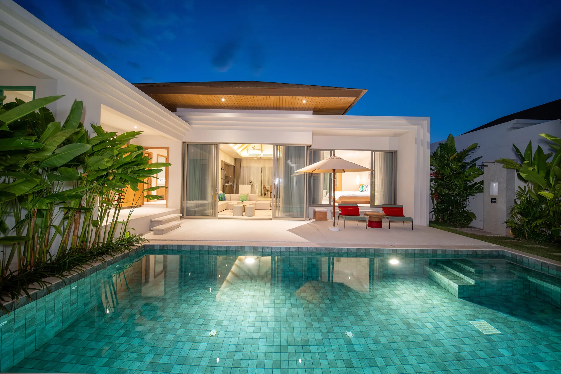 Private pool at dusk, lit from below, in front of the single-storey villa with its living room open to the terrace