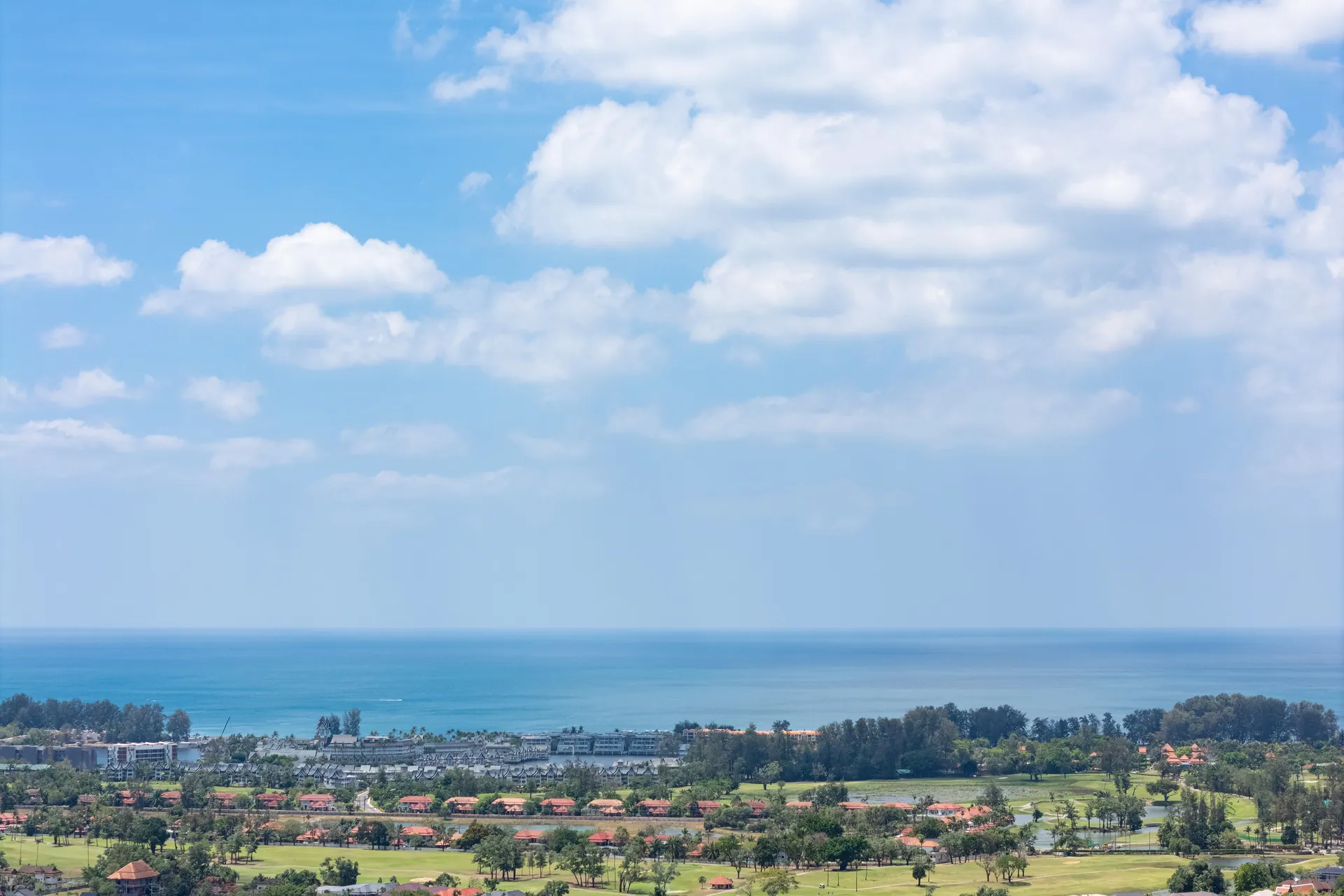 Drone view from high above the area, over a golf course and low-rise resorts towards the sea