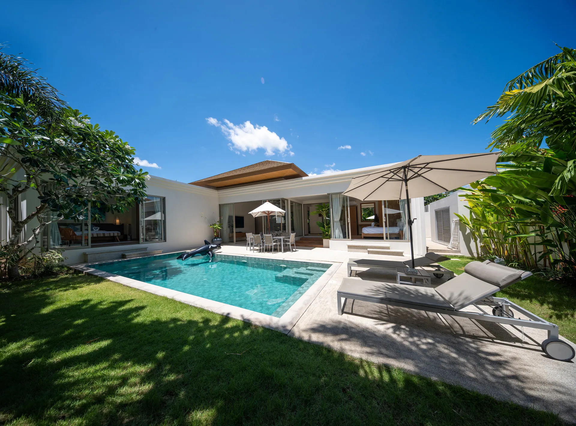 The villa and pool by day, with a lawn, sun loungers and a large parasol