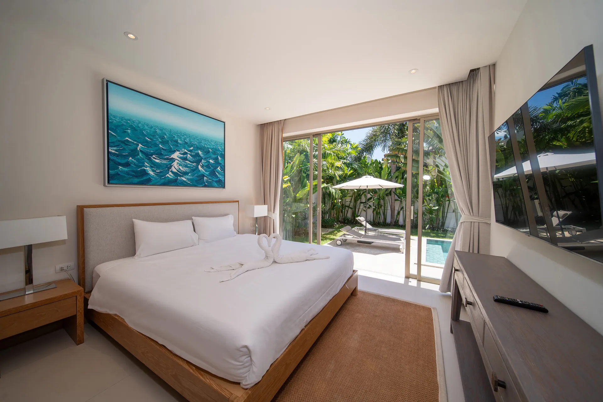 Bedroom with an ocean painting above the bed and sliding glass doors onto the pool garden