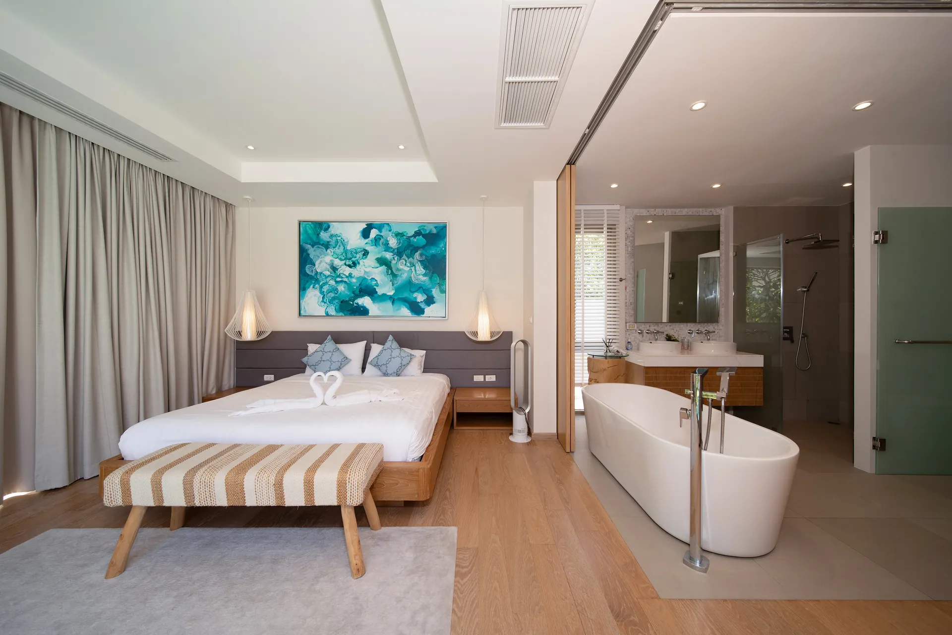 Main bedroom with a large bed, a striped bench and a freestanding bathtub in the open en-suite
