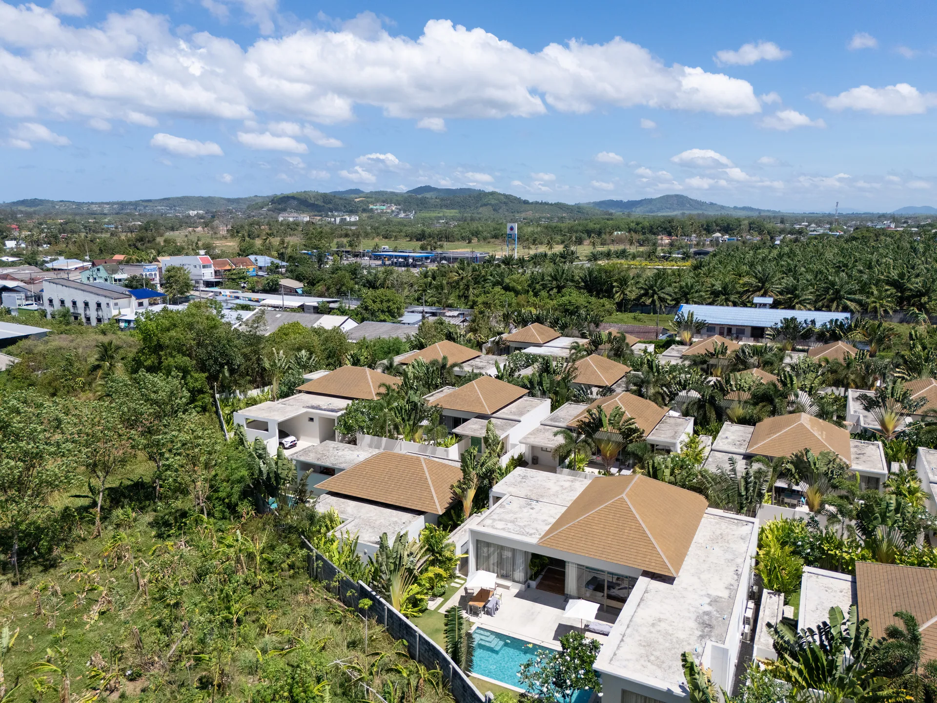 Aerial view of the villa community on a green hillside, with the hills of Phuket behind