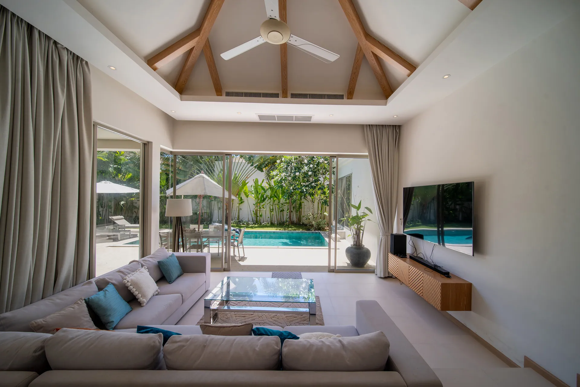 Living room with a sunken sofa, a vaulted timber-beamed ceiling and glass doors to the pool