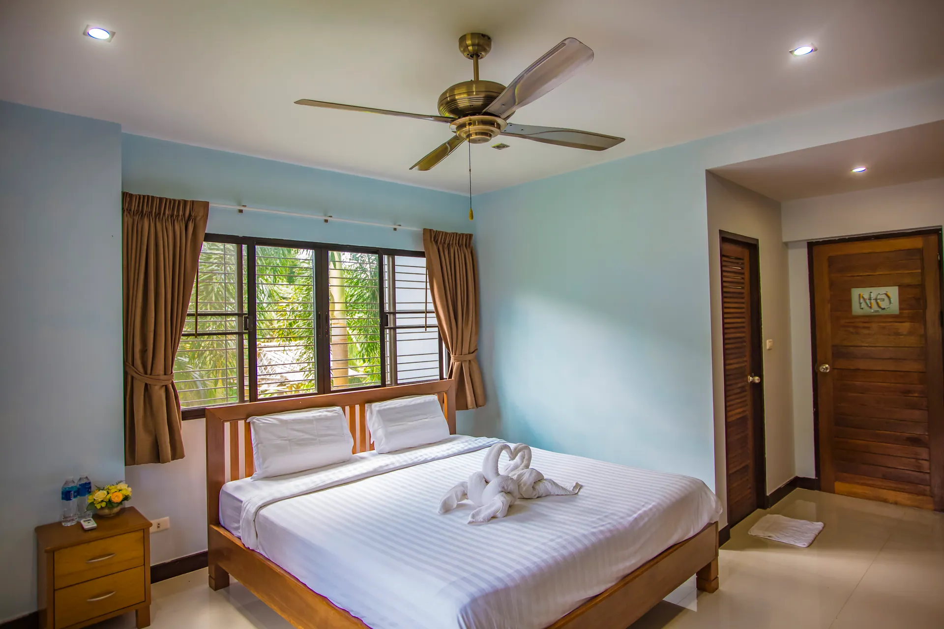 Bedroom with a timber double bed, a bedside table and a ceiling fan, with windows onto the garden