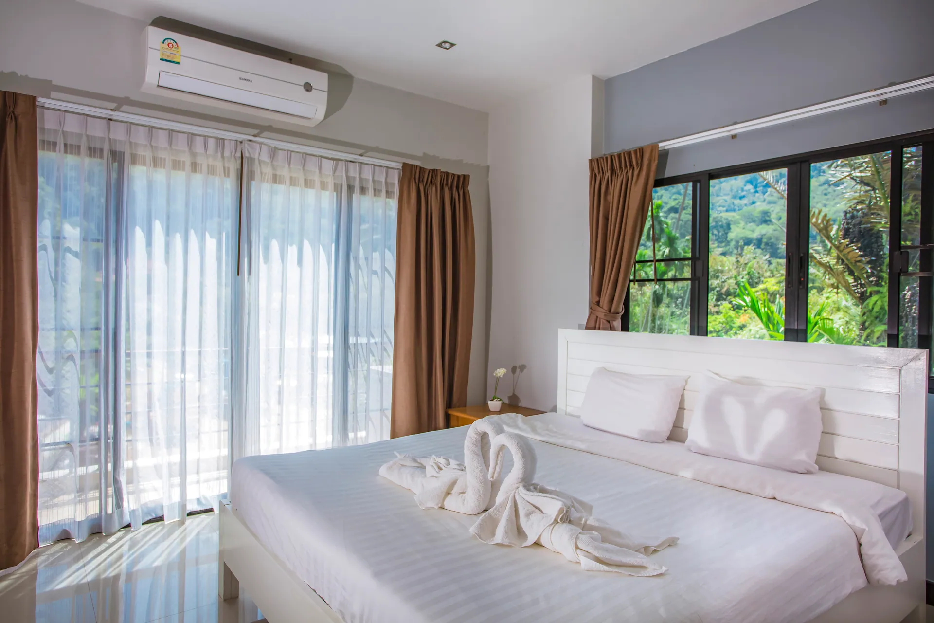 Bedroom with a white panelled headboard, air conditioning and sheer-curtained glass doors