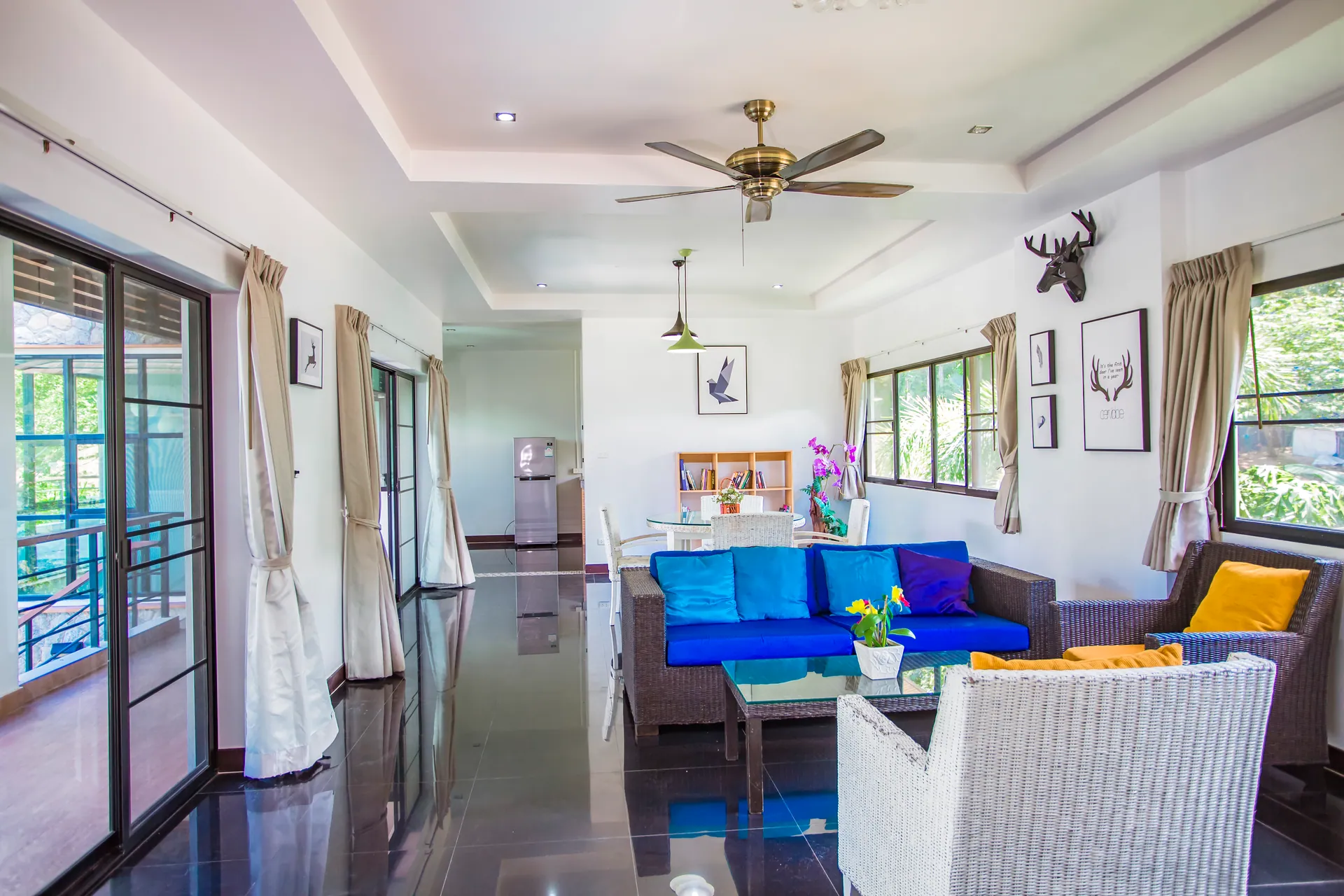 Living room with blue-cushioned rattan sofas, white wicker armchairs, a ceiling fan and glass doors to a balcony